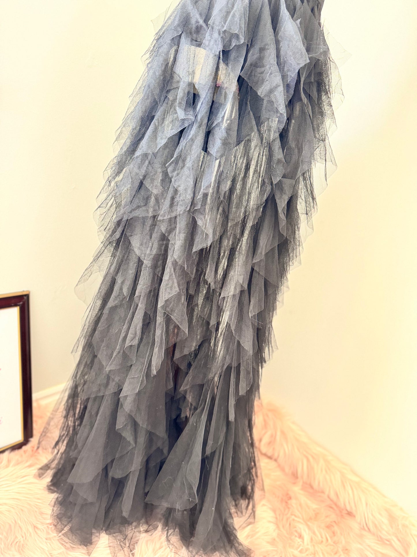 Introducing an black tulle gown that exudes timeless sophistication and drama. Featuring a structured, deep V-cut bodice that enhances the silhouette, this piece is designed with a sleek bodysuit bottom for a flawless, sculpted fit. The fitted waistline flows into cascading layers of soft, ruffled tulle, creating a breathtaking, ethereal effect with every step. This beautifully rehomed gown carries a story of style and elegance, ready to be cherished by its next wearer.