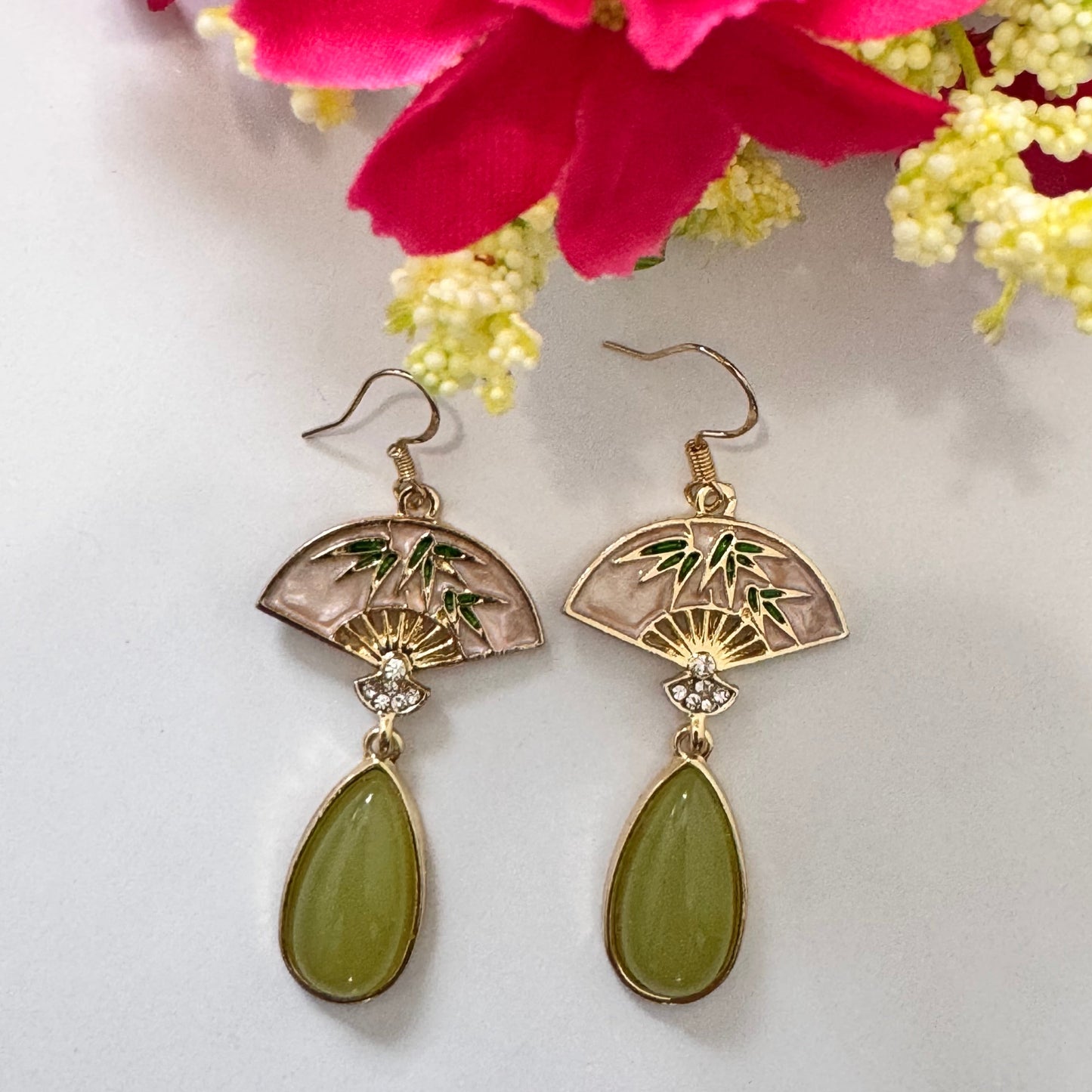 Step into a world of sophisticated charm with these exquisite Oriental Fan Drop Earrings, blending cultural elegance with modern allure. Featuring a delicate gold-toned fan motif, adorned with bamboo details and sparkling crystal accents, these earrings exude grace and refinement.