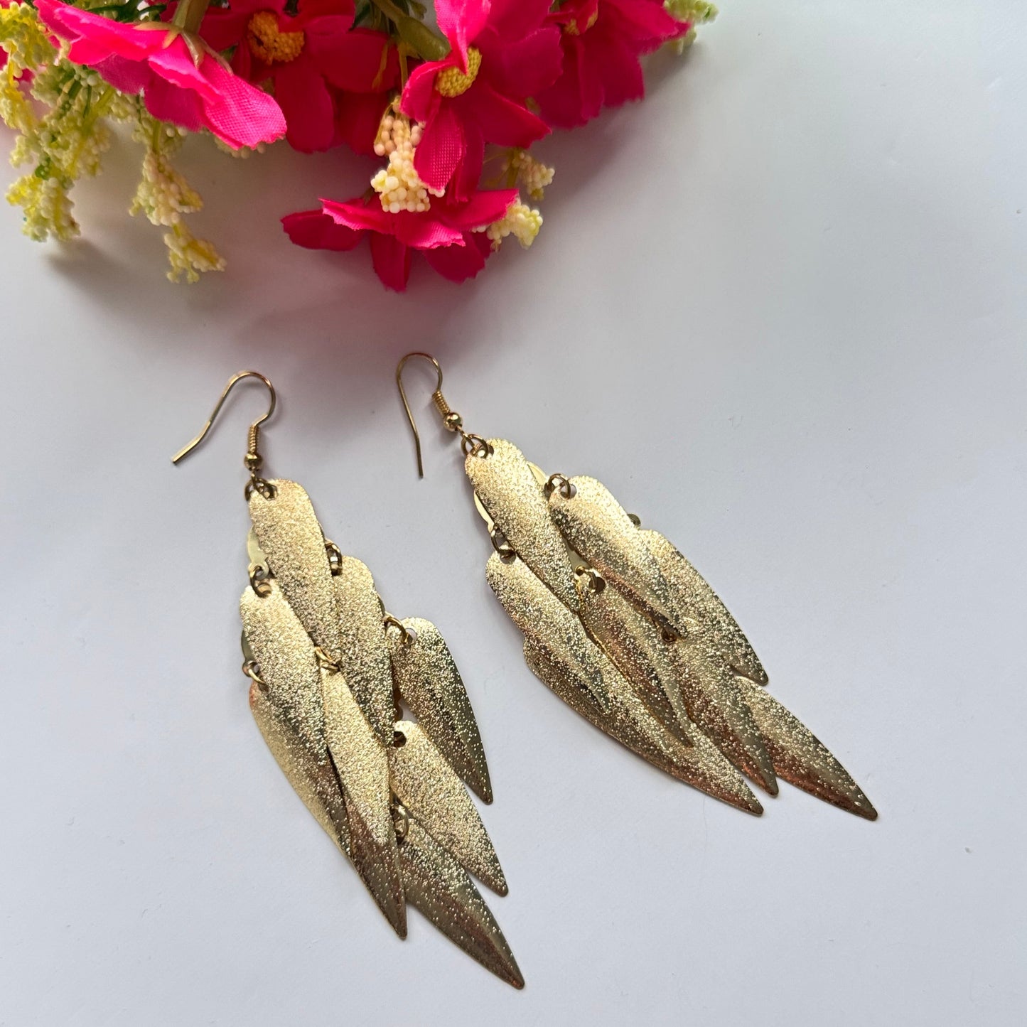 Stunning gold-toned statement earrings, designed to captivate and command attention. Featuring a cascading arrangement of textured metallic leaf-like elements, these lightweight yet bold earrings exude elegance, movement, and a touch of glamour.