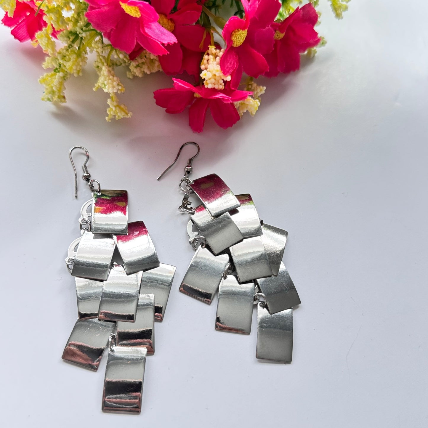 Elevate your style with these captivating silver statement earrings, designed to turn heads with their unique cascading geometric design. Crafted with a dynamic arrangement of reflective metallic squares, they catch the light with every movement, creating an irresistible shimmer. These ultra-chic dangles exude modern elegance with a touch of edgy sophistication, making them the perfect accessory for any occasion, from glamorous nights out to stylish daytime looks.