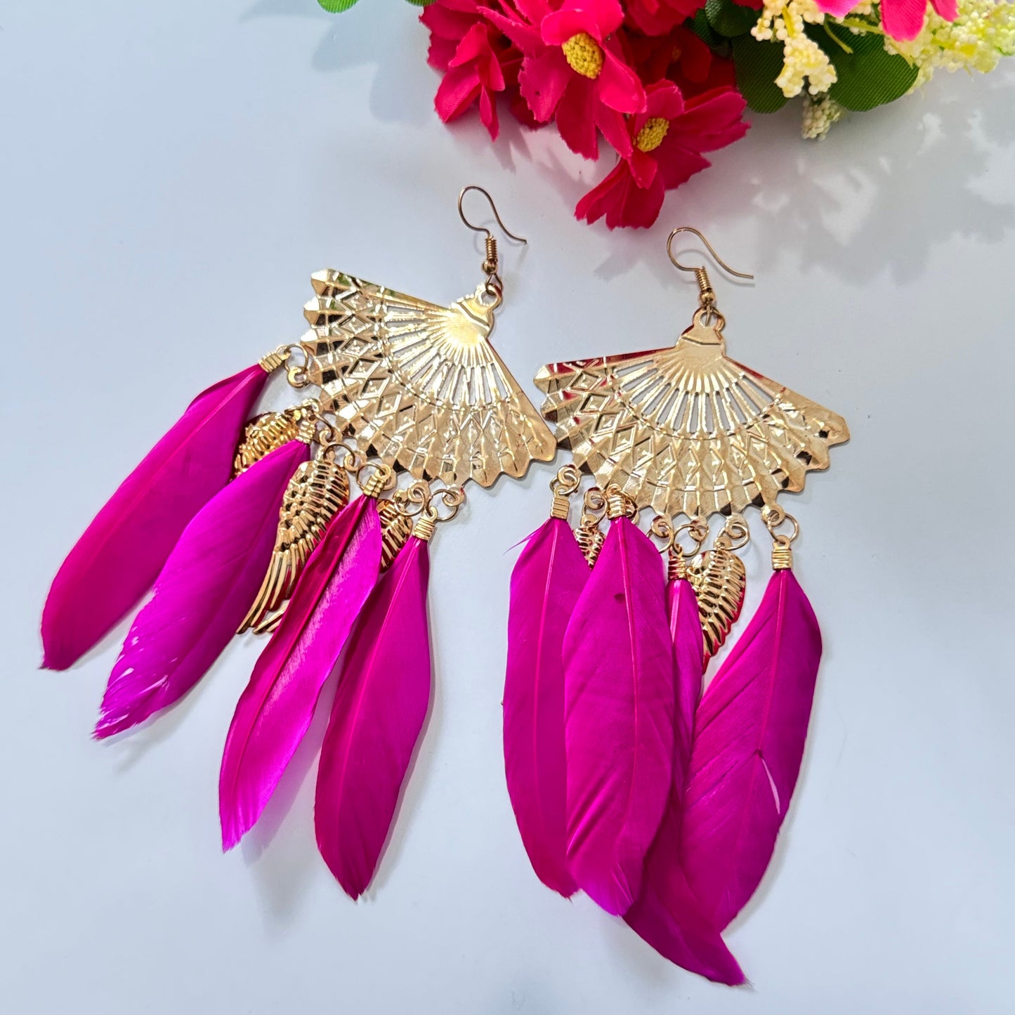 These breathtaking fan-shaped gold earrings feature intricate detailing, exuding a luxurious charm that captivates at first glance. Adorned with vibrant feather accents in striking red and fuchsia hues, they add a dramatic flair to any outfit, making them perfect for fashion-forward people who love to stand out.