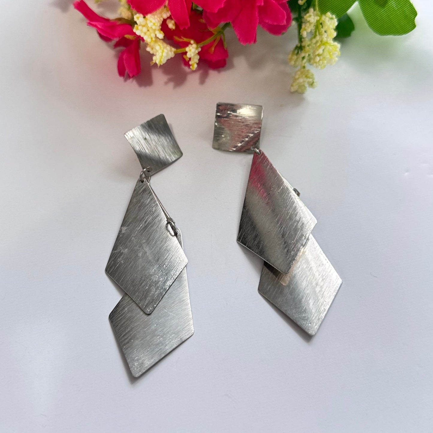 Make a sleek and sophisticated statement with these stunning silver-tone geometric drop earrings, designed to add a modern edge to any outfit. Featuring a cascading arrangement of brushed metal diamond-shaped panels, these earrings create an effortlessly chic and dynamic look.