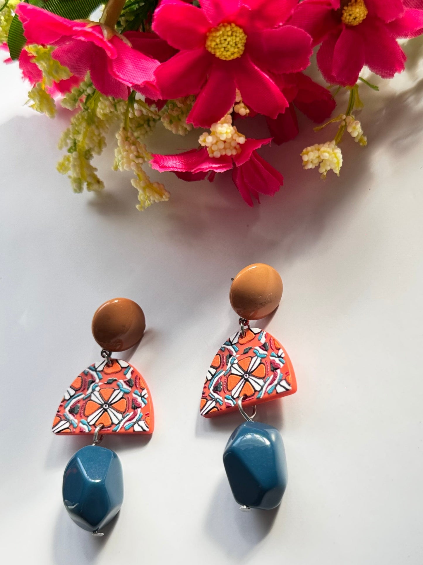 Add a bold statement to your style with these statement earrings, designed to captivate attention with their unique fusion of earthy tones and vibrant artistry. Featuring a warm caramel-toned stud, a geometric charm with intricate patterns in fiery orange, white, and black, and a deep blue faceted bead that adds a touch of sophistication, these earrings are a masterpiece of color harmony and texture. Lightweight yet impactful, they bring a perfect balance of modern elegance and artistic flair to any outfit.