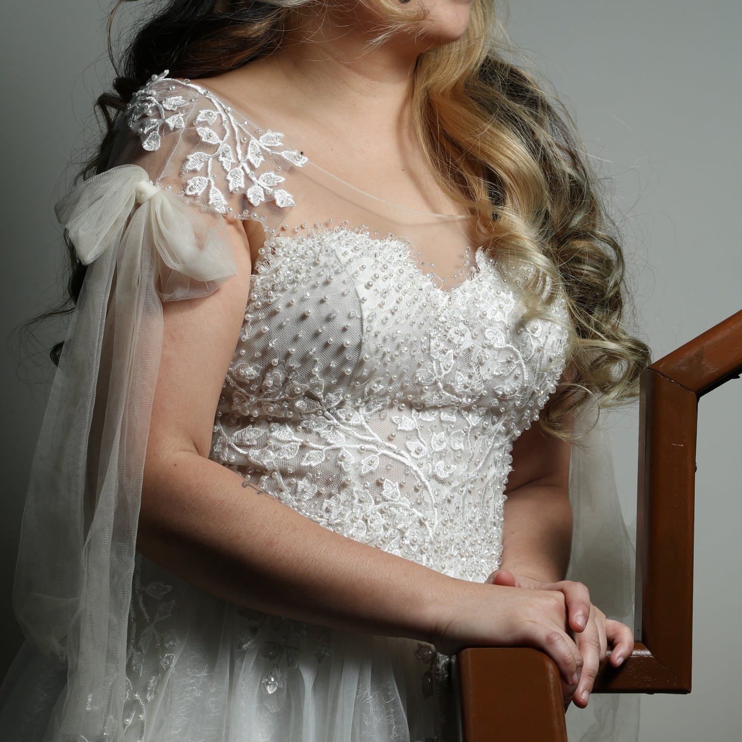 This is a light, ethereal wedding dress featuring delicate floral embroidery and beadwork. The gown has an off-the-shoulder design with sheer tulle straps tied into bows, adding a romantic touch. The bodice is adorned with intricate pearl and lace detailing, while the flowing tulle skirt is embellished with embroidered leaves, creating an elegant and whimsical look.