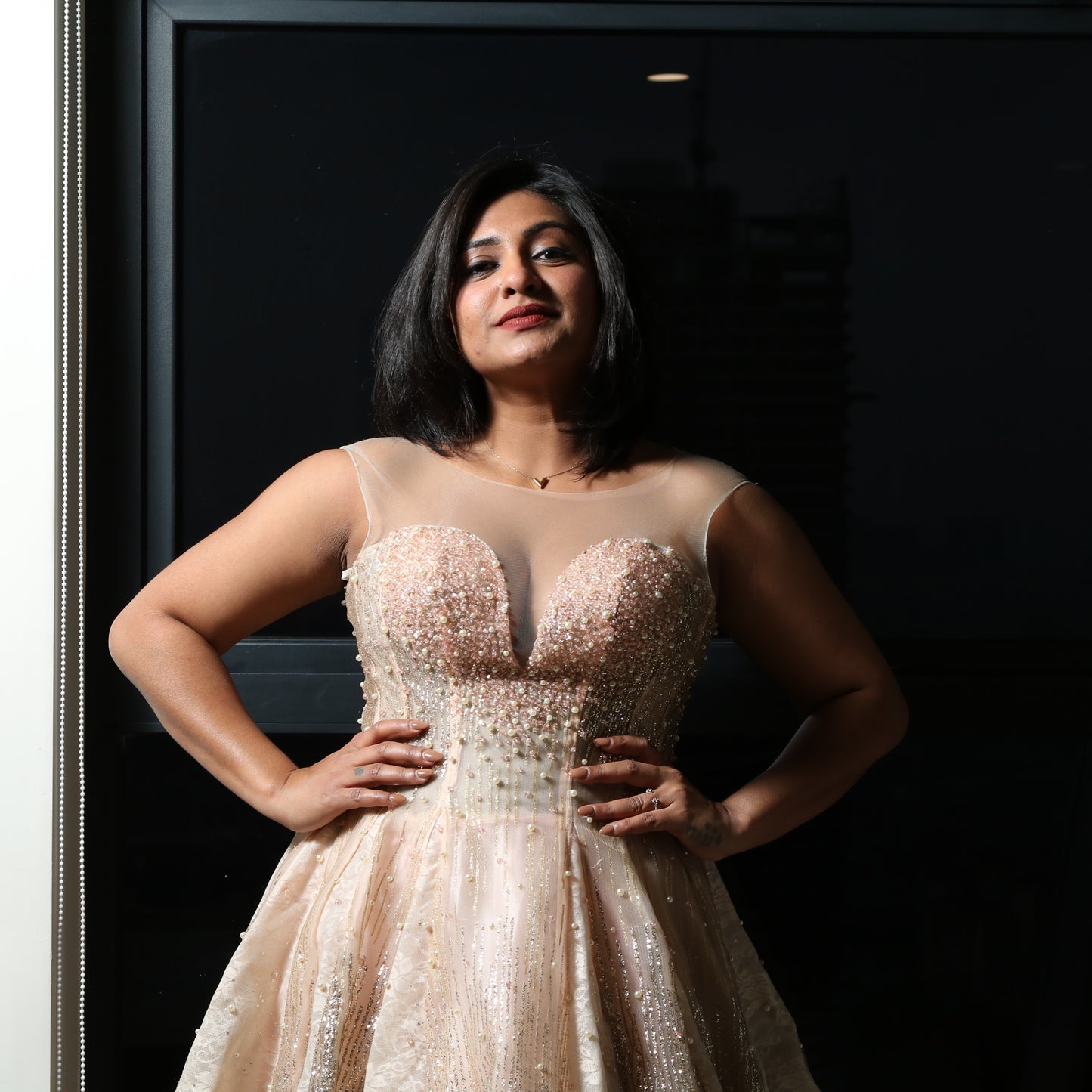 The dress in the image is an elegant, heavily embellished gown with a fitted bodice and a voluminous skirt. It features intricate beadwork and embroidery, giving it a luxurious and opulent look. The sheer illusion neckline adds a delicate touch, while the structured, corset-like bodice enhances the silhouette. The fabric appears to be thick and richly adorned, making the dress quite heavy. The overall design exudes a regal and glamorous feel, perfect for a formal event or gala.