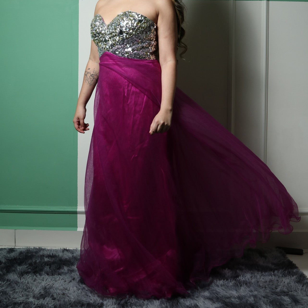 This dress features a strapless, sweetheart neckline bodice adorned with reflective silver embellishments, creating a glamorous and eye-catching effect. The voluminous skirt is made of rich magenta tulle, adding an elegant and dramatic touch. The combination of sparkle and flowy fabric makes it a perfect choice for formal events or evening wear.