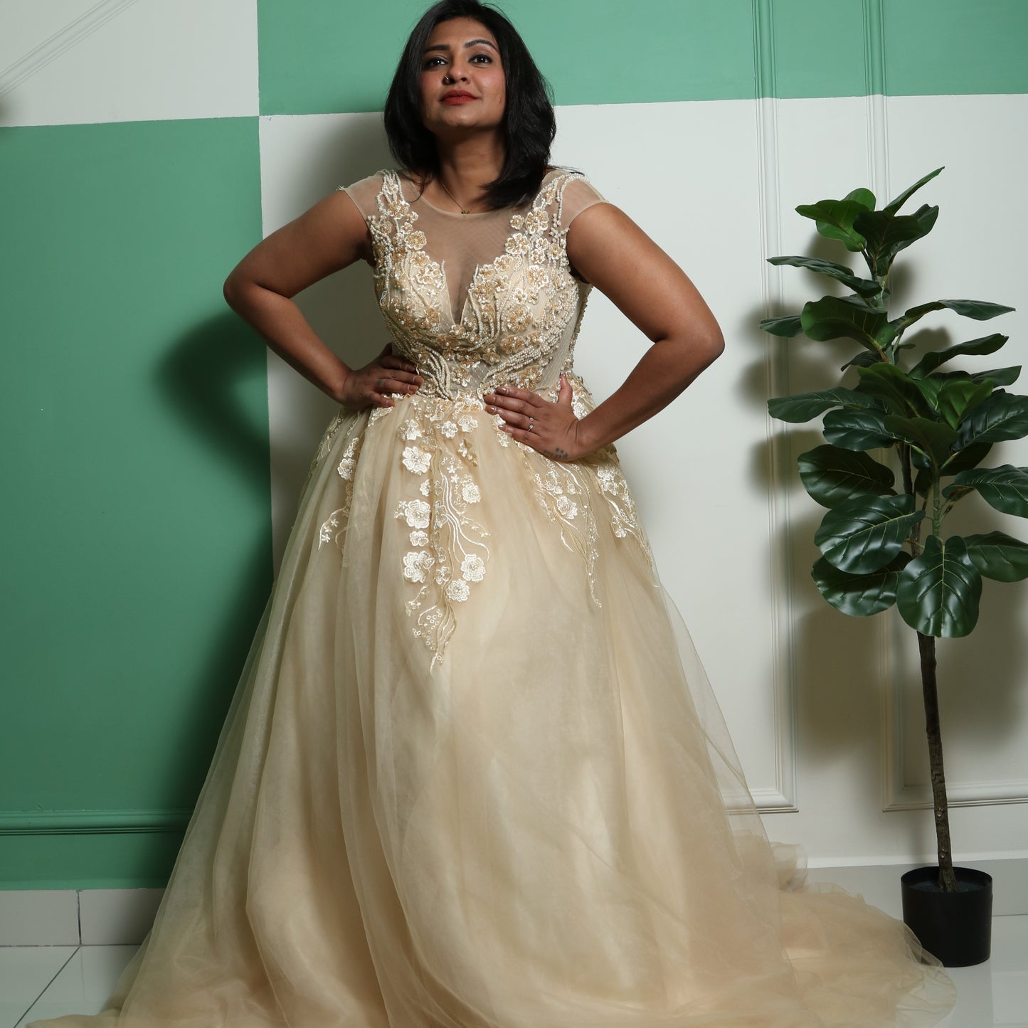 The dress in the image is a floor-length gown in a soft champagne or gold color. It features a fitted bodice with intricate floral embroidery and beadwork, extending into delicate cap sleeves. The gown has a sheer illusion neckline, adding elegance and sophistication. The voluminous tulle skirt flows gracefully, creating a princess-like silhouette. This dress is perfect for formal events, weddings, or special occasions.