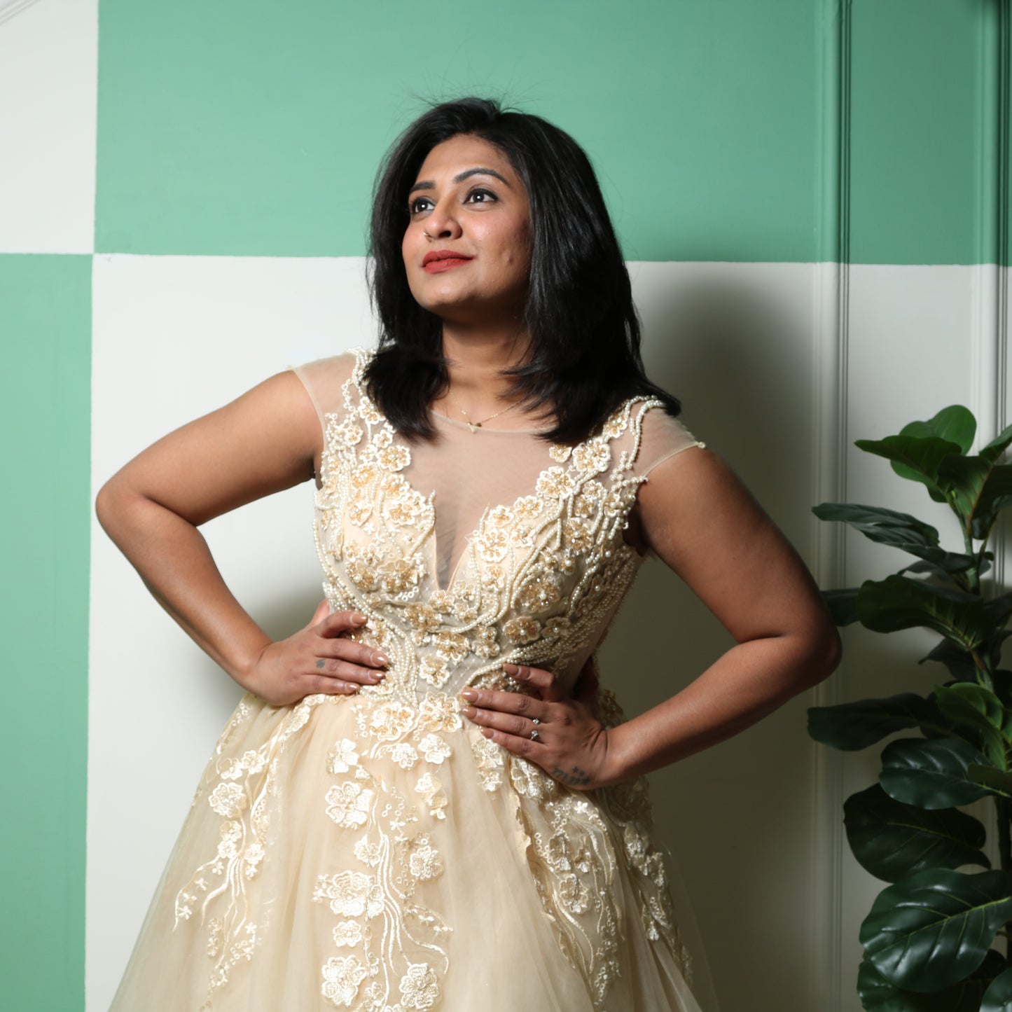 The dress in the image is a floor-length gown in a soft champagne or gold color. It features a fitted bodice with intricate floral embroidery and beadwork, extending into delicate cap sleeves. The gown has a sheer illusion neckline, adding elegance and sophistication. The voluminous tulle skirt flows gracefully, creating a princess-like silhouette. This dress is perfect for formal events, weddings, or special occasions.