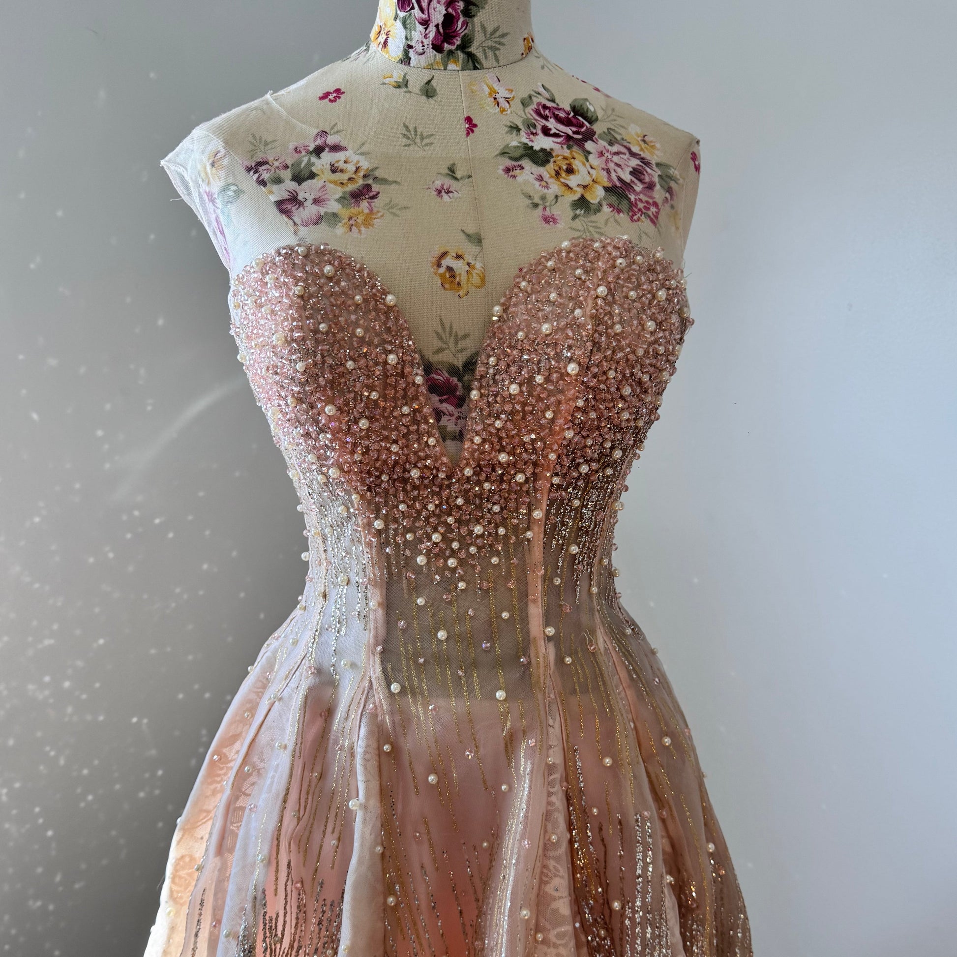 The dress is an elegant, heavily embellished gown with a fitted bodice and a voluminous skirt. It features intricate beadwork and embroidery, giving it a luxurious and opulent look. The sheer illusion neckline adds a delicate touch, while the structured, corset-like bodice enhances the silhouette. The fabric appears to be thick and richly adorned, making the dress quite heavy. The overall design exudes a regal and glamorous feel, perfect for a formal event or gala.