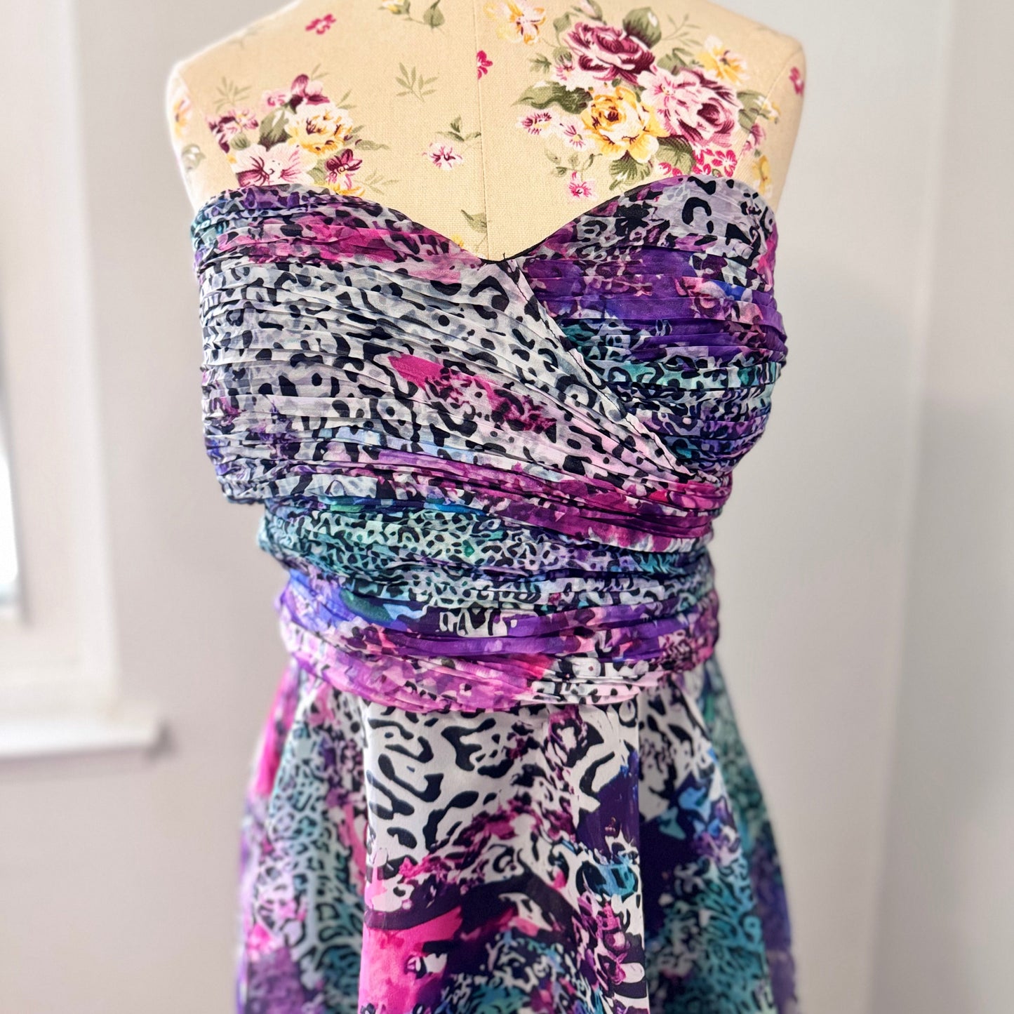 Unleash your bold, vibrant spirit with this breathtaking strapless gown, a mesmerizing fusion of art and fashion. Designed to turn heads, this flowing masterpiece features an explosion of rich purples, electric blues, and striking pinks in a captivating abstract animal print. The ruched bodice flatters the silhouette, while the voluminous skirt cascades effortlessly, creating a dreamy, ethereal effect with every step. 
