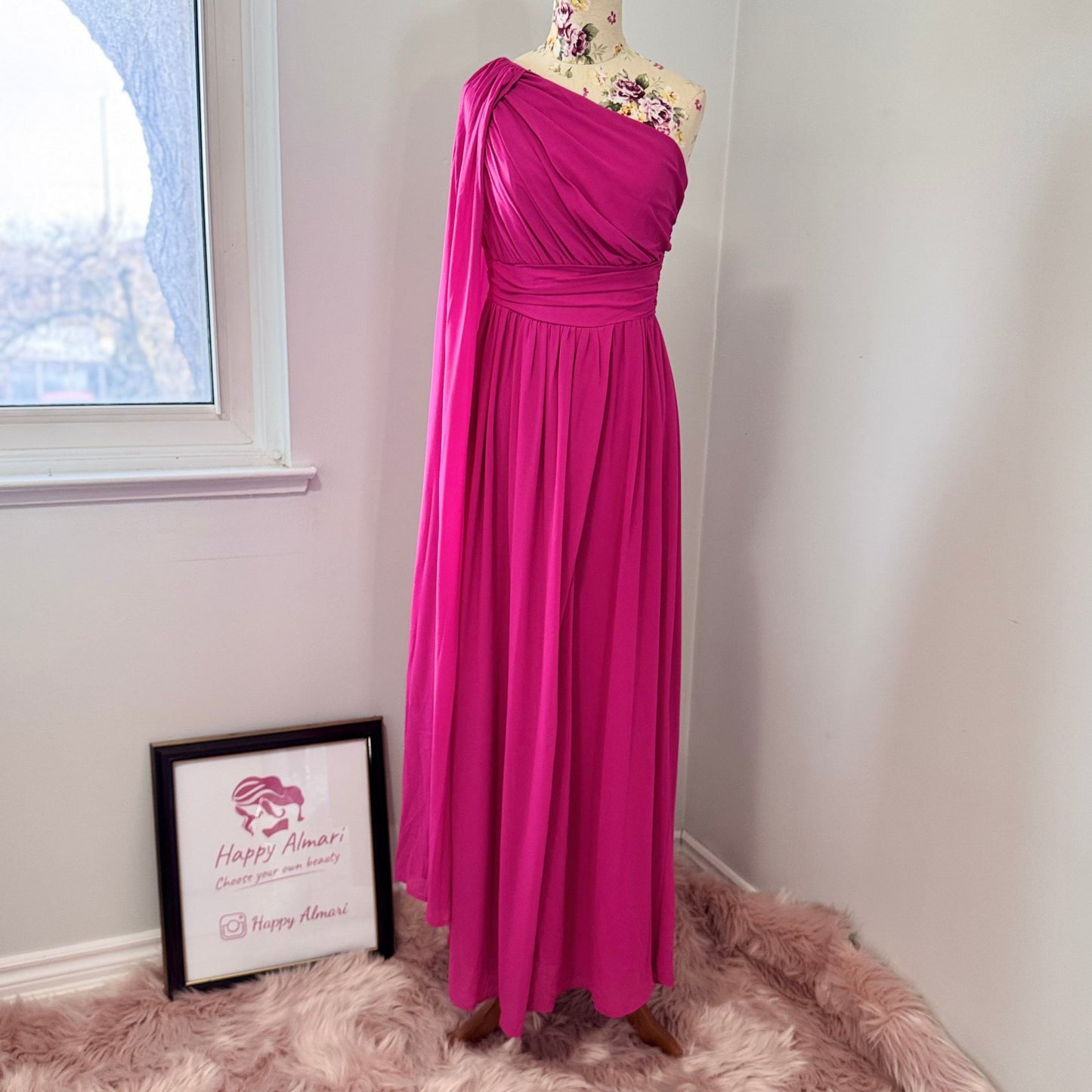 Step into effortless elegance with this breathtaking fuchsia one-shoulder gown, designed to make a statement at any event. Featuring a gracefully draped sleeve that cascades like a flowing waterfall, this dress exudes confidence, sophistication, and timeless charm. The cinched waist enhances your silhouette, while the soft, flowing fabric moves beautifully with every step.
