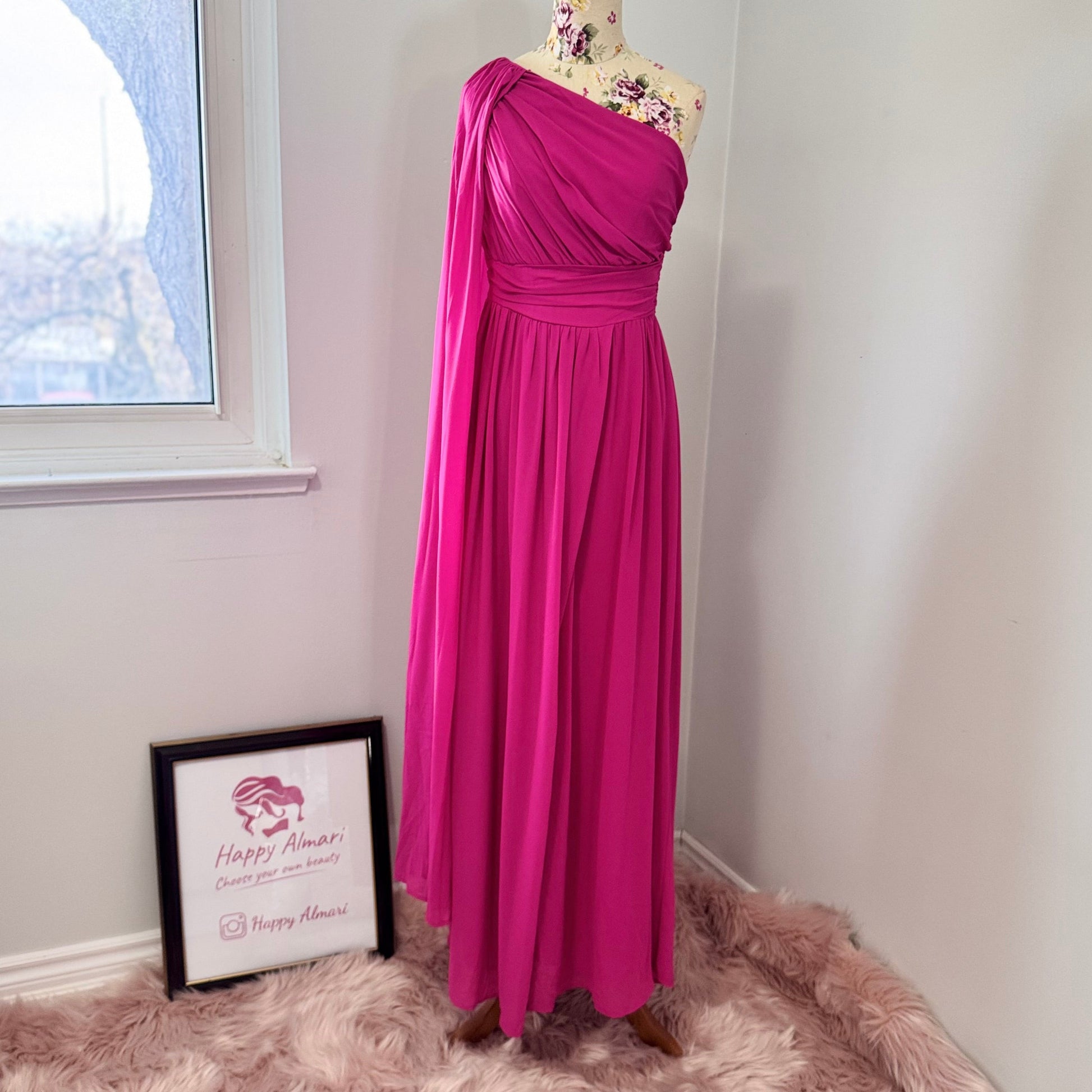 Step into effortless elegance with this breathtaking fuchsia one-shoulder gown, designed to make a statement at any event. Featuring a gracefully draped sleeve that cascades like a flowing waterfall, this dress exudes confidence, sophistication, and timeless charm. The cinched waist enhances your silhouette, while the soft, flowing fabric moves beautifully with every step.