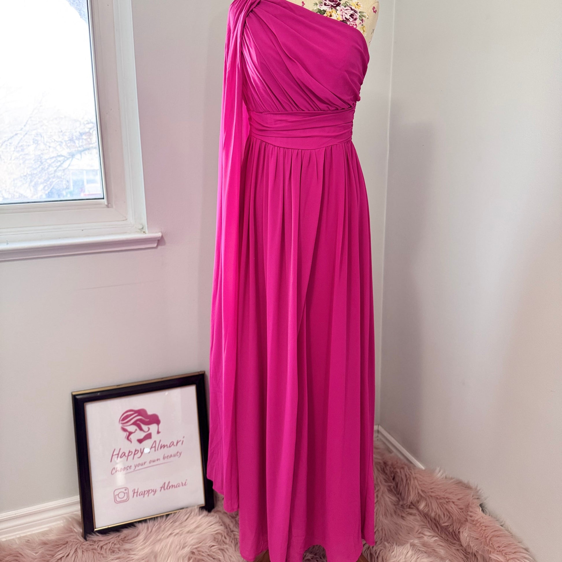 Step into effortless elegance with this breathtaking fuchsia one-shoulder gown, designed to make a statement at any event. Featuring a gracefully draped sleeve that cascades like a flowing waterfall, this dress exudes confidence, sophistication, and timeless charm. The cinched waist enhances your silhouette, while the soft, flowing fabric moves beautifully with every step.