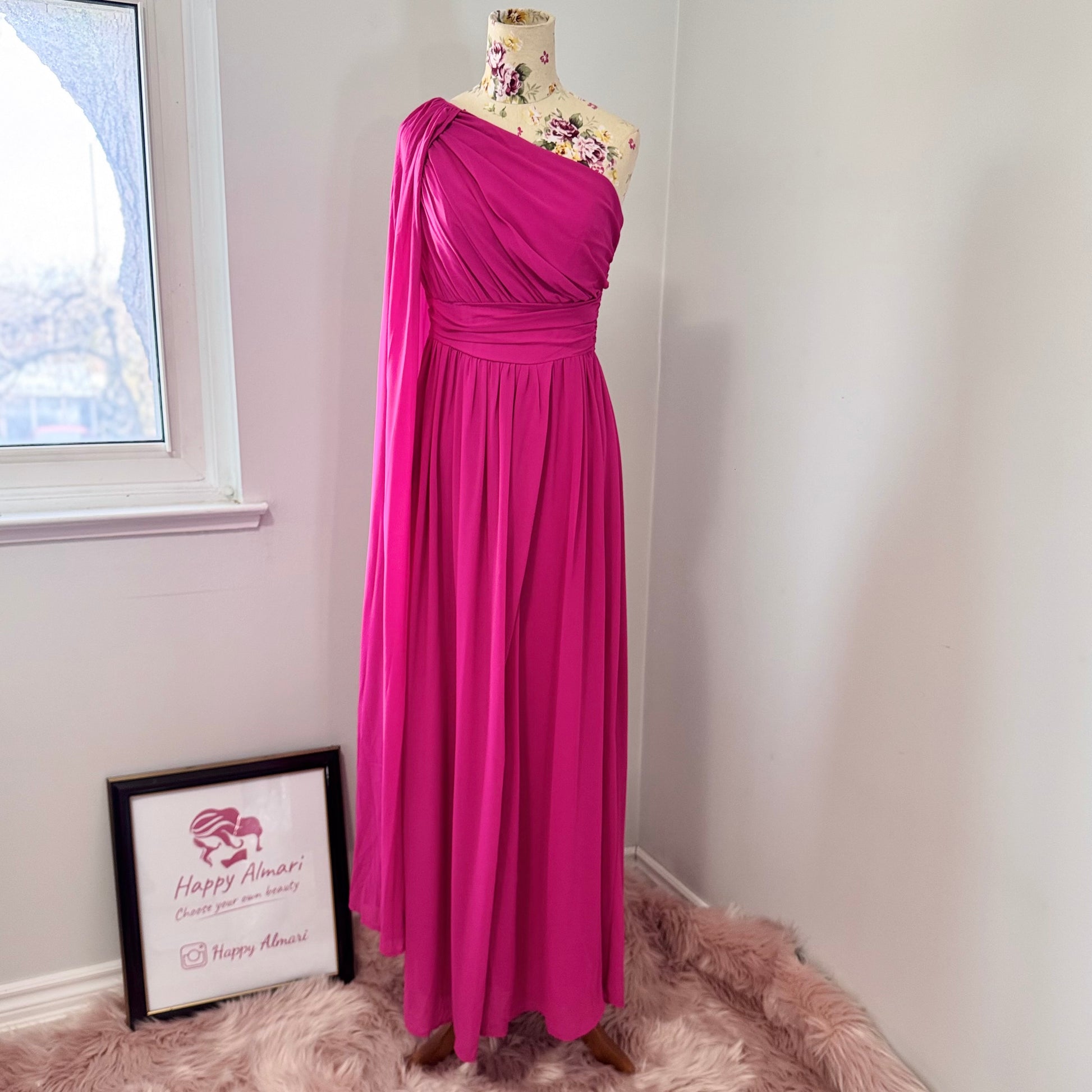 Step into effortless elegance with this breathtaking fuchsia one-shoulder gown, designed to make a statement at any event. Featuring a gracefully draped sleeve that cascades like a flowing waterfall, this dress exudes confidence, sophistication, and timeless charm. The cinched waist enhances your silhouette, while the soft, flowing fabric moves beautifully with every step.
