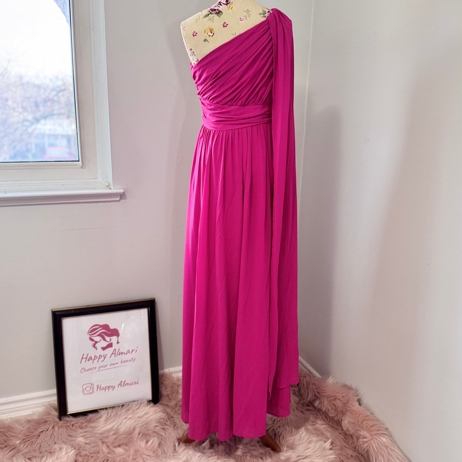 Step into effortless elegance with this breathtaking fuchsia one-shoulder gown, designed to make a statement at any event. Featuring a gracefully draped sleeve that cascades like a flowing waterfall, this dress exudes confidence, sophistication, and timeless charm. The cinched waist enhances your silhouette, while the soft, flowing fabric moves beautifully with every step.