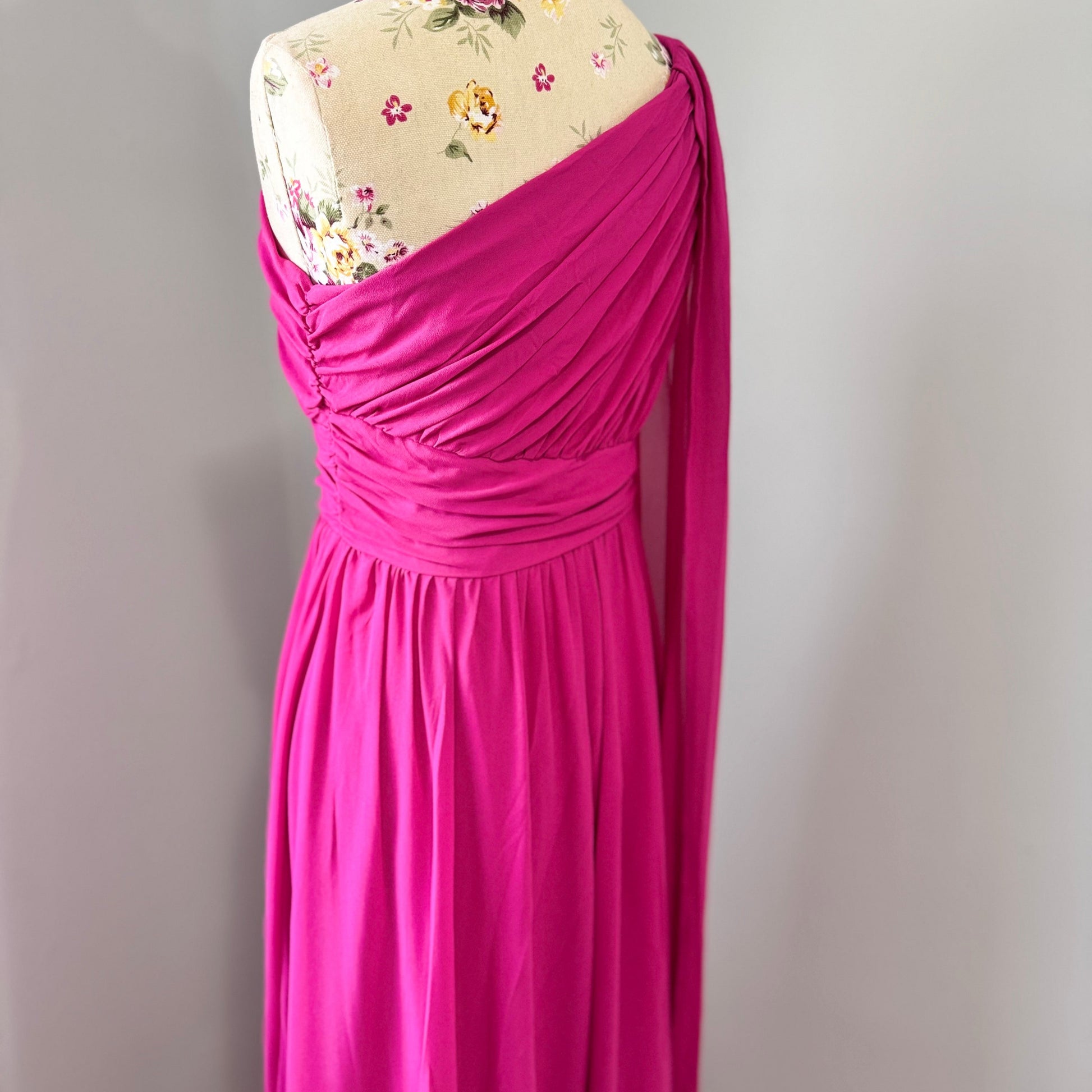 Step into effortless elegance with this breathtaking fuchsia one-shoulder gown, designed to make a statement at any event. Featuring a gracefully draped sleeve that cascades like a flowing waterfall, this dress exudes confidence, sophistication, and timeless charm. The cinched waist enhances your silhouette, while the soft, flowing fabric moves beautifully with every step.