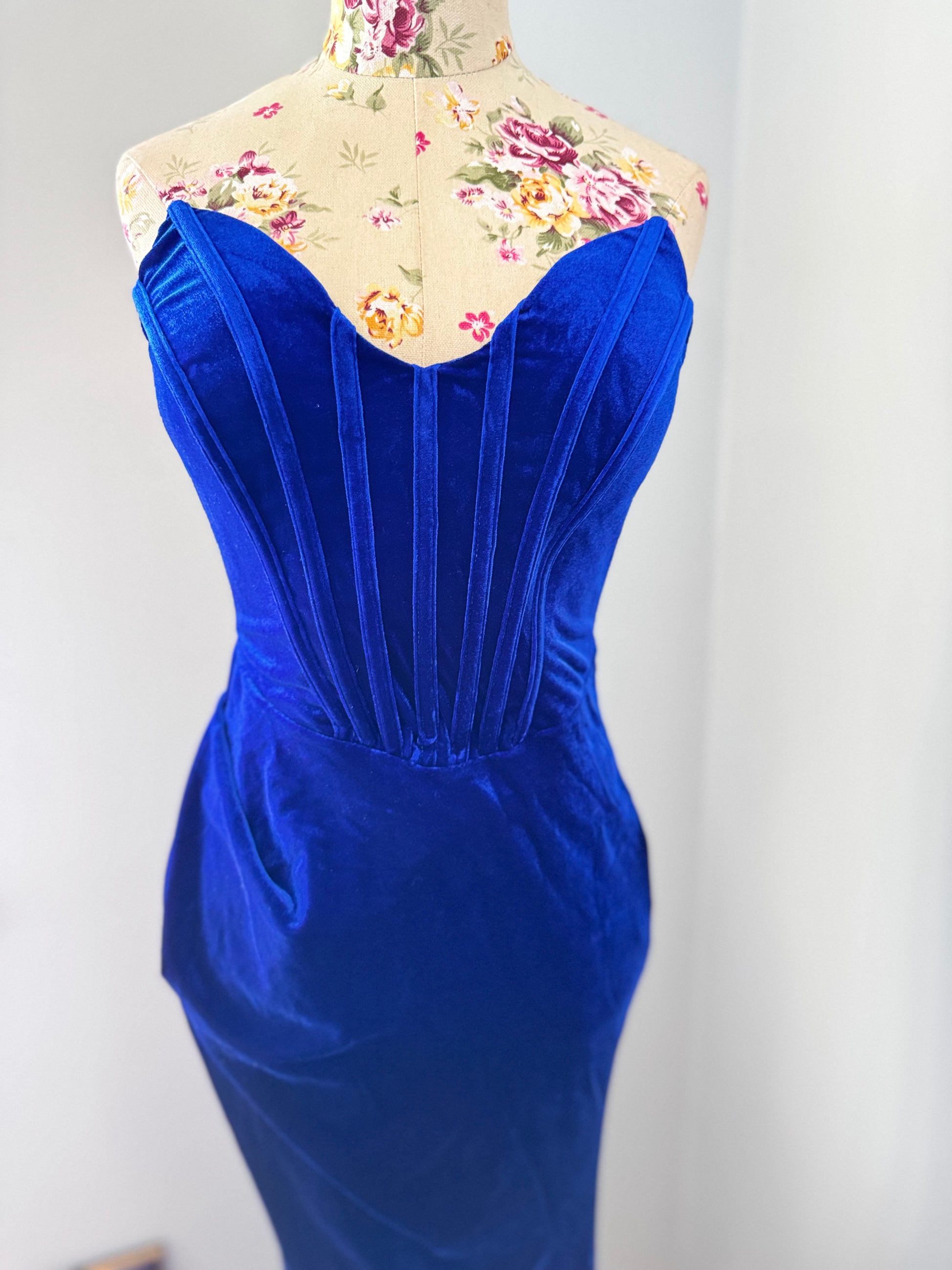 Step into timeless elegance with this breathtaking previously cherished royal blue velvet evening gown, designed to turn heads at any event. Crafted from rich, ultra-soft velvet, this figure-hugging masterpiece features a structured corset bodice with delicate pleated detailing that accentuates your silhouette. The sweetheart neckline adds a touch of romance, while the flowing skirt with a sultry thigh-high slit creates the perfect balance of sophistication and allure. In perfect condition.