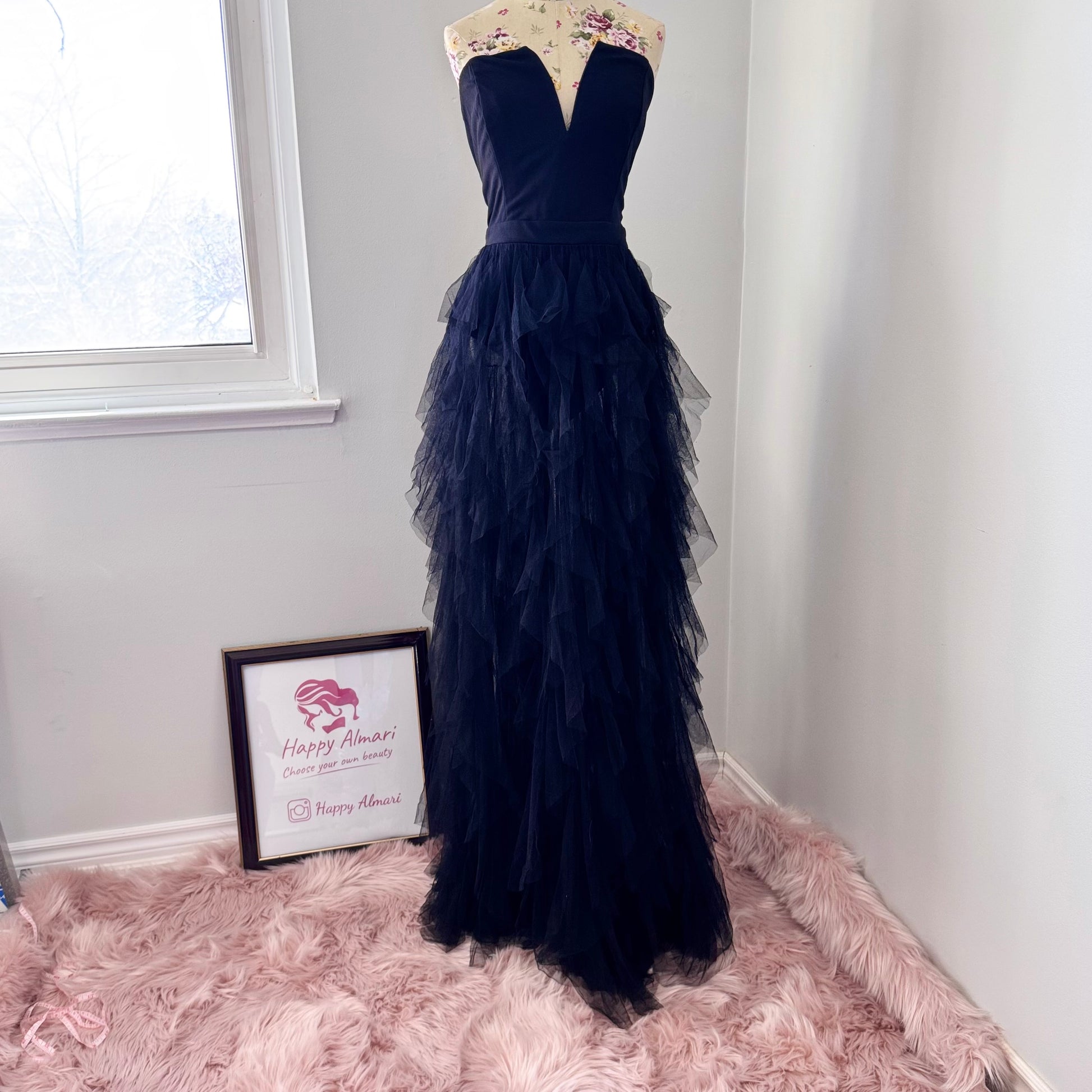 Introducing an black tulle gown that exudes timeless sophistication and drama. Featuring a structured, deep V-cut bodice that enhances the silhouette, this piece is designed with a sleek bodysuit bottom for a flawless, sculpted fit. The fitted waistline flows into cascading layers of soft, ruffled tulle, creating a breathtaking, ethereal effect with every step. This beautifully rehomed gown carries a story of style and elegance, ready to be cherished by its next wearer.