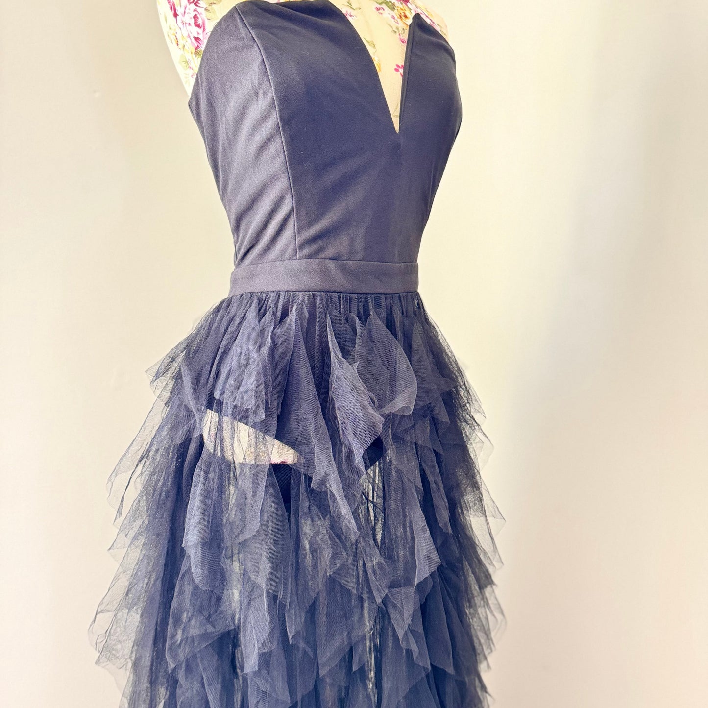 Introducing an black tulle gown that exudes timeless sophistication and drama. Featuring a structured, deep V-cut bodice that enhances the silhouette, this piece is designed with a sleek bodysuit bottom for a flawless, sculpted fit. The fitted waistline flows into cascading layers of soft, ruffled tulle, creating a breathtaking, ethereal effect with every step. This beautifully rehomed gown carries a story of style and elegance, ready to be cherished by its next wearer.