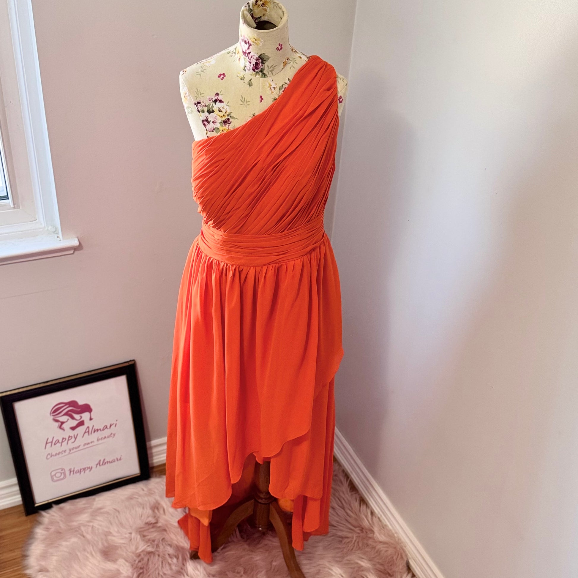 Turn heads with this stunning one-shoulder asymmetrical gown in a bold, fiery orange hue! Designed to make a statement, this dress features intricate pleating across the bodice for a flattering fit, a cinched waist that accentuates your curves, and a flowing high-low skirt that moves beautifully with every step.