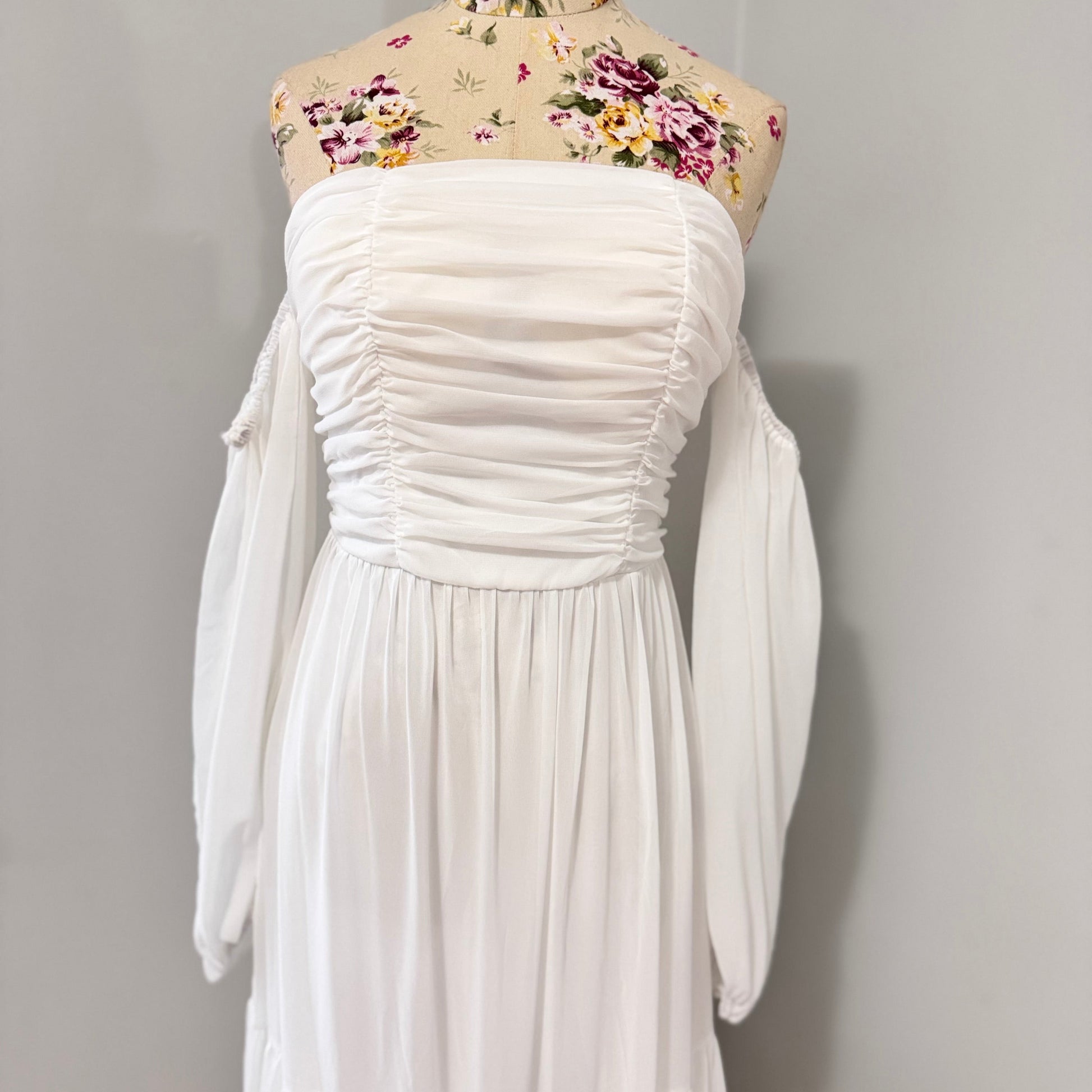 Step into effortless elegance with this stunning off-shoulder white maxi dress, designed to make you feel like a goddess at any event! Featuring a flattering ruched bodice, romantic flowy tiered skirt, and long billowy sleeves.