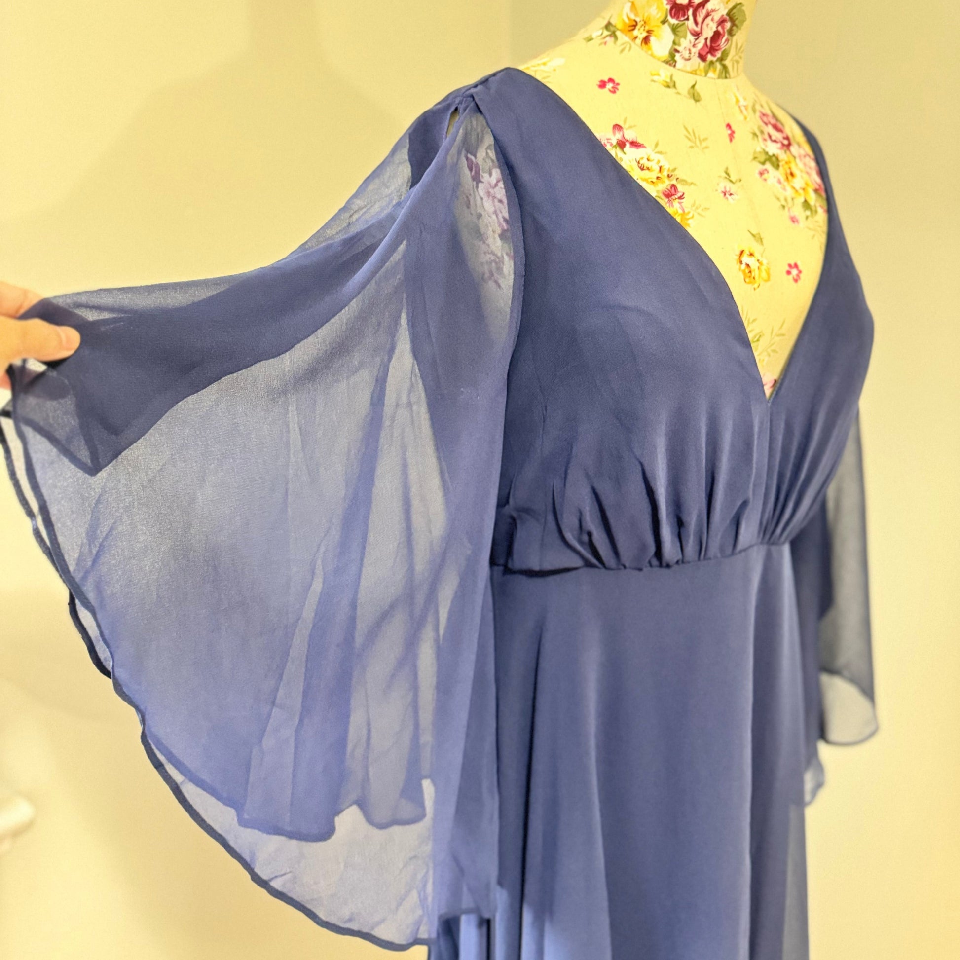 Turn heads in this stunning deep navy gown that radiates elegance and grace. Designed with a flowy chiffon overlay, a flattering cinched waist, and dreamy flutter sleeves, this dress is perfect for formal events, weddings, or special occasions. The deep V-neckline and subtle front slit add just the right touch of sophistication and allure. This gently cherished piece is in excellent condition, ready for a new owner to make unforgettable memories.