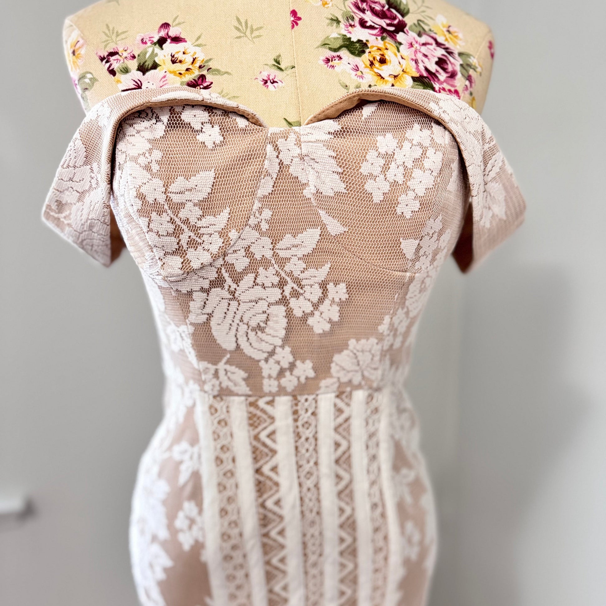 This breathtaking off-shoulder lace gown is designed to captivate with its intricate floral lace detailing and figure-enhancing silhouette. The delicate sheer bodice, complemented by a soft nude underlayer, creates a stunning contrast, while the high-low lace hemline adds a touch of modern romance.
