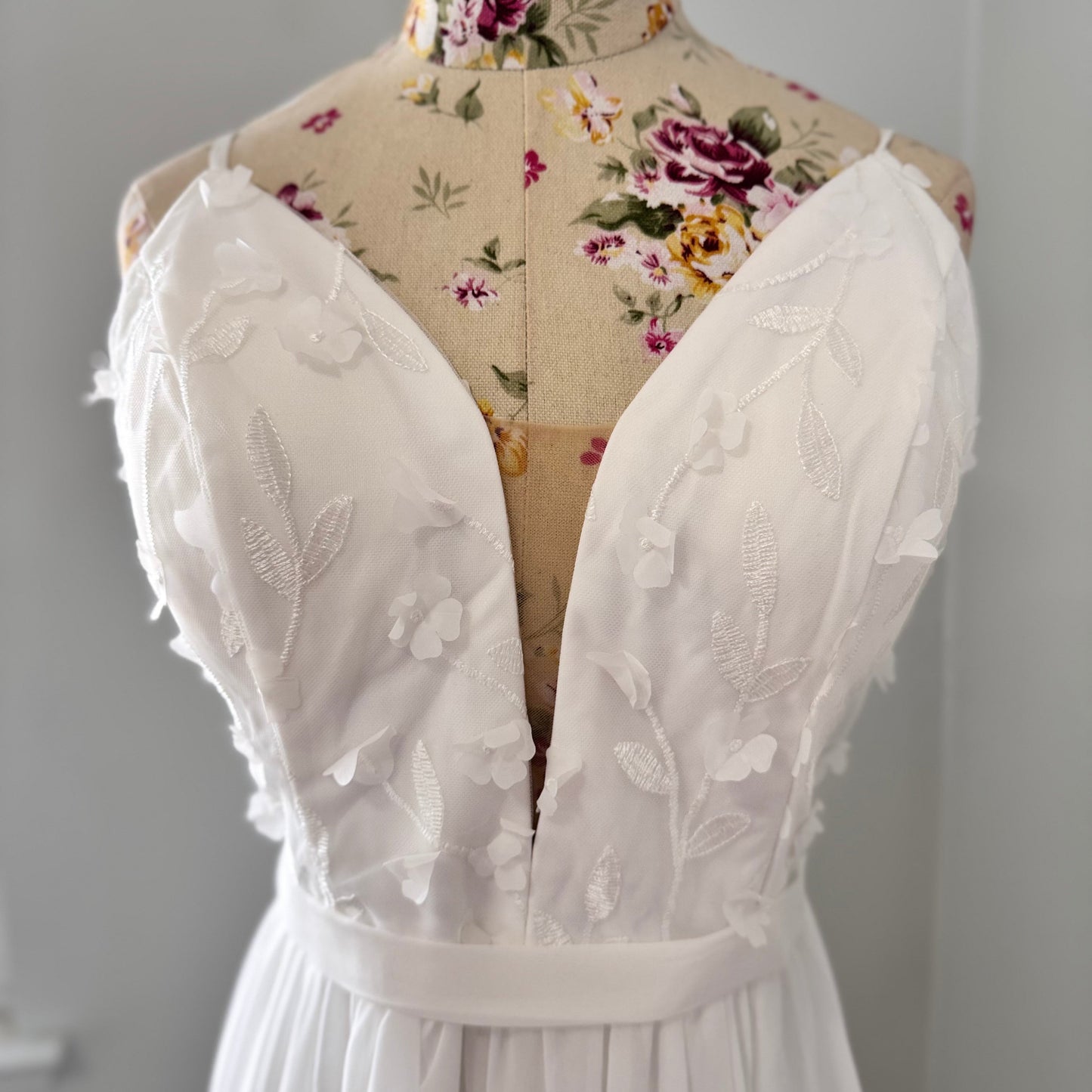 Elevate your style with this breathtaking white gown, designed to captivate with its effortless elegance and timeless charm. Featuring a flowy A-line silhouette, this dress showcases a delicate plunging V-neckline adorned with intricate 3D floral appliqués and embroidered leaf details, adding a soft, ethereal touch. The fitted bodice seamlessly transitions into a lightweight, flowing chiffon skirt, creating graceful movement with every step.