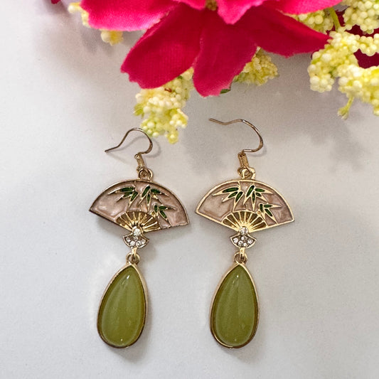 Step into a world of sophisticated charm with these exquisite Oriental Fan Drop Earrings, blending cultural elegance with modern allure. Featuring a delicate gold-toned fan motif, adorned with bamboo details and sparkling crystal accents, these earrings exude grace and refinement.