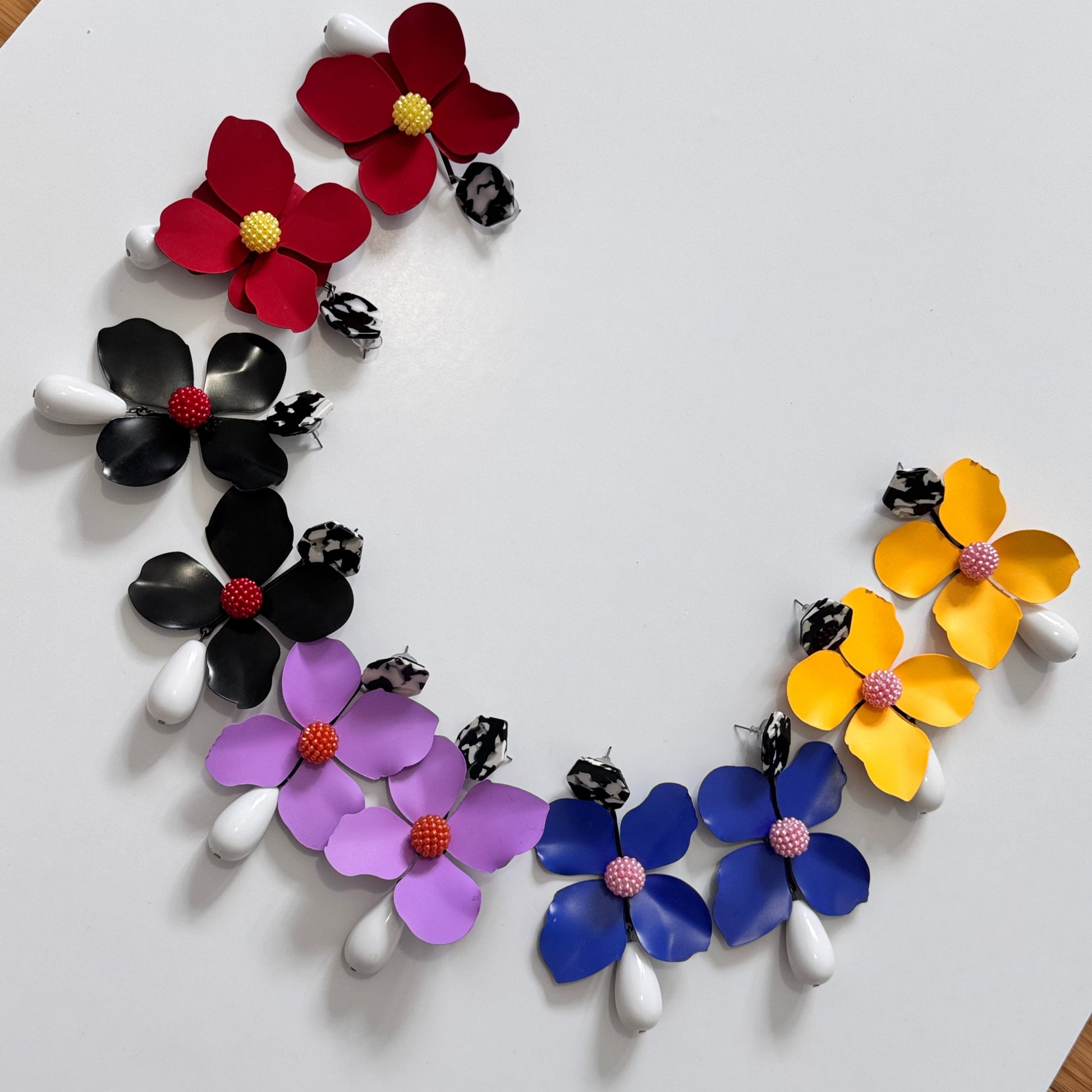 Add a bold pop of color to your look with these stunning floral drop earrings! hese earrings feature delicately sculpted flowers in rich hues of red, black, lilac, royal blue, and sunshine yellow, accented with textured centers for a playful yet sophisticated touch. 