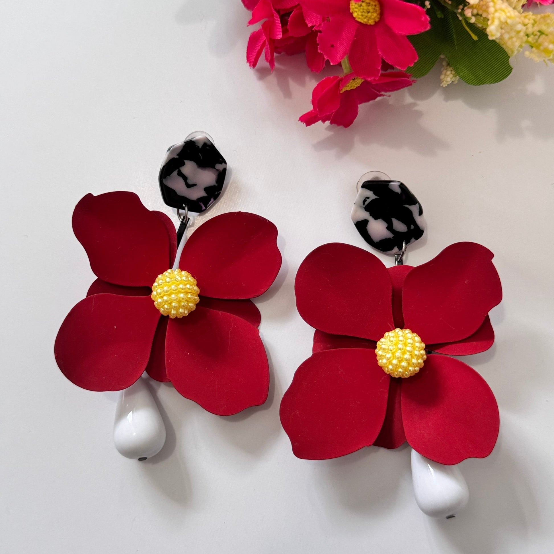 Add a bold pop of color to your look with these stunning floral drop earrings! hese earrings feature delicately sculpted flowers in rich hues of red, black, lilac, royal blue, and sunshine yellow, accented with textured centers for a playful yet sophisticated touch. 