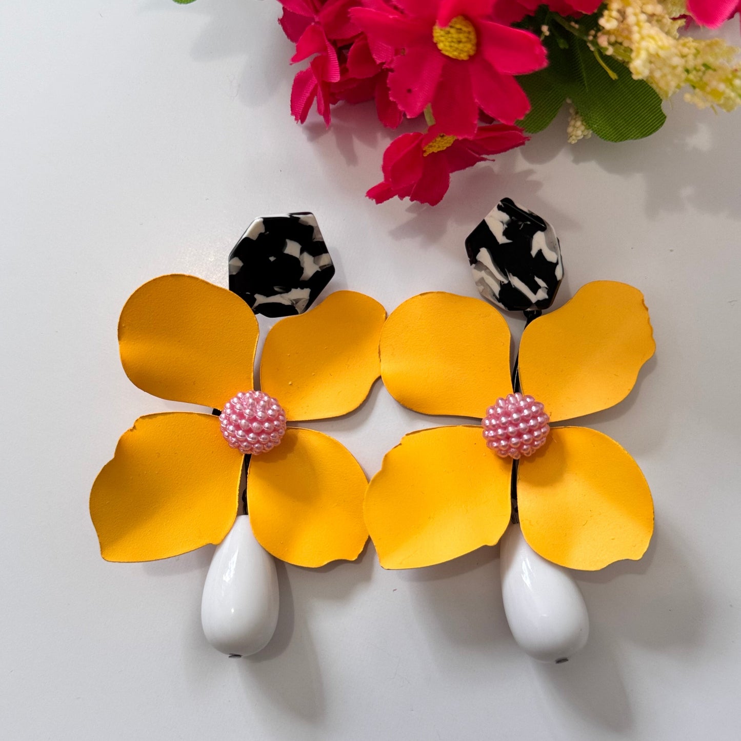 Add a bold pop of color to your look with these stunning floral drop earrings! hese earrings feature delicately sculpted flowers in rich hues of red, black, lilac, royal blue, and sunshine yellow, accented with textured centers for a playful yet sophisticated touch. 