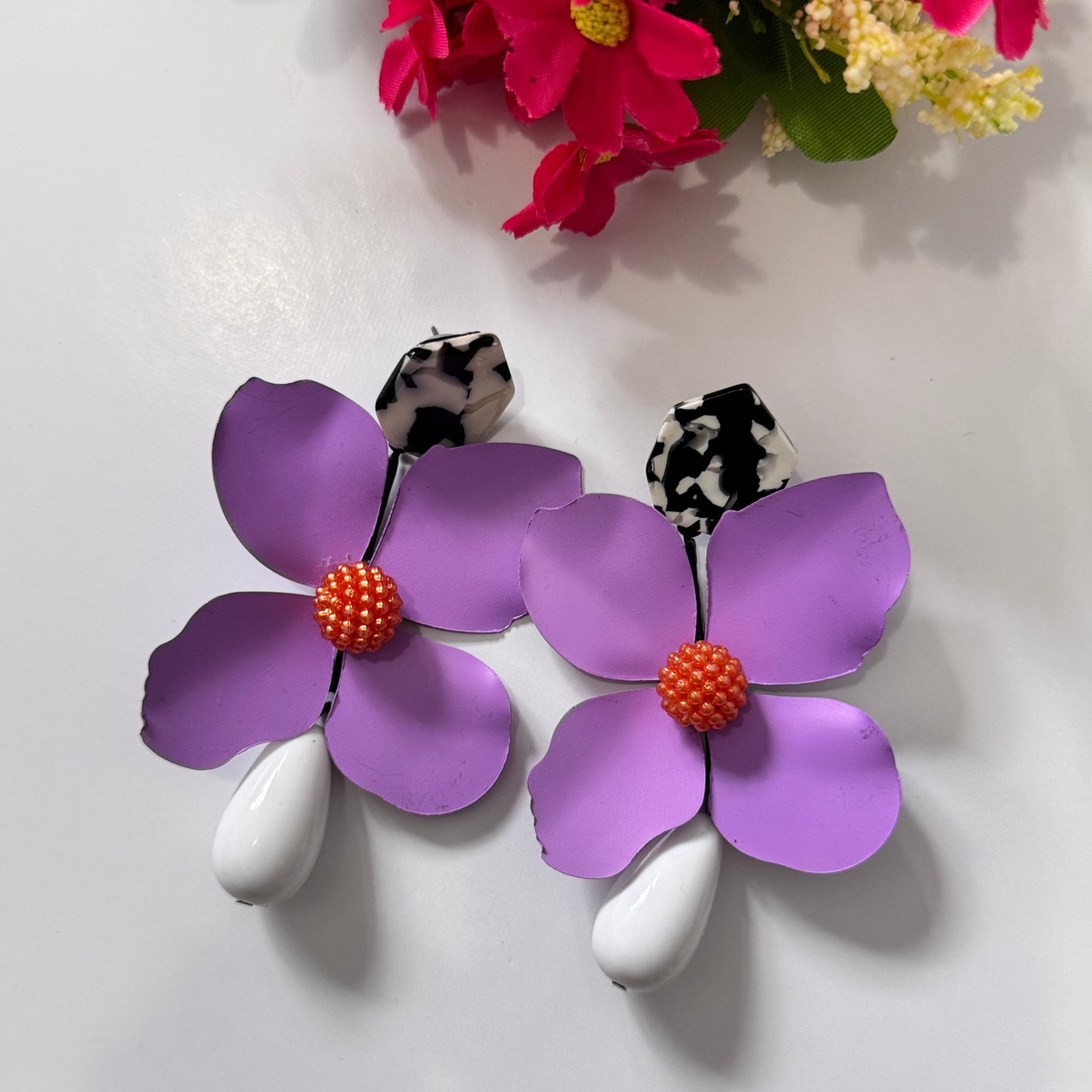 Add a bold pop of color to your look with these stunning floral drop earrings! hese earrings feature delicately sculpted flowers in rich hues of red, black, lilac, royal blue, and sunshine yellow, accented with textured centers for a playful yet sophisticated touch. 