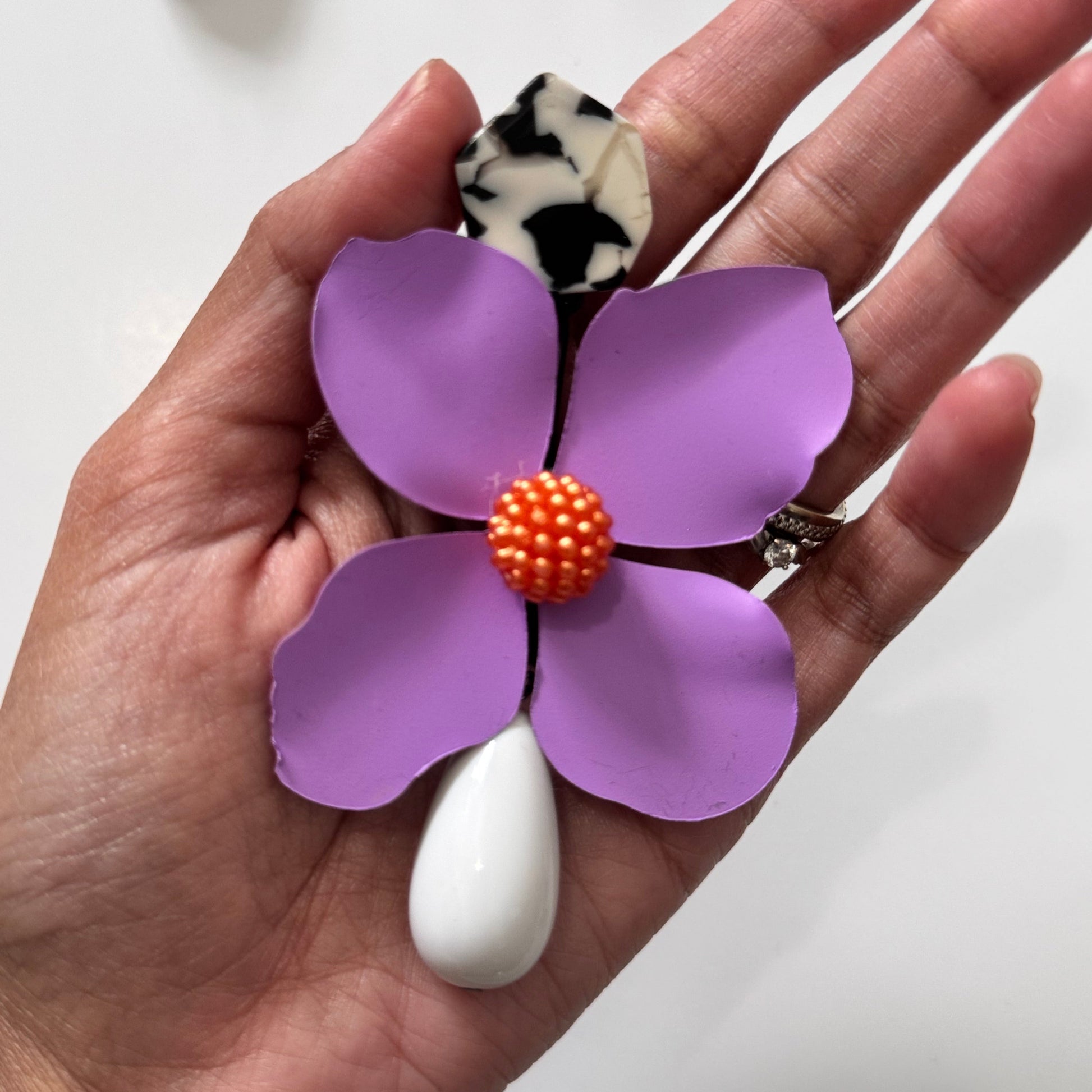 Add a bold pop of color to your look with these stunning floral drop earrings! hese earrings feature delicately sculpted flowers in rich hues of red, black, lilac, royal blue, and sunshine yellow, accented with textured centers for a playful yet sophisticated touch. 