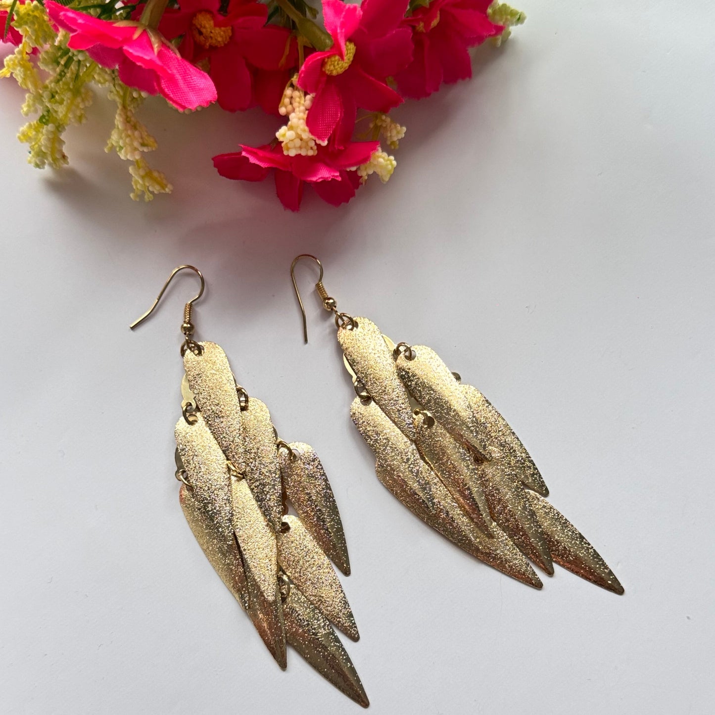 Stunning gold-toned statement earrings, designed to captivate and command attention. Featuring a cascading arrangement of textured metallic leaf-like elements, these lightweight yet bold earrings exude elegance, movement, and a touch of glamour.