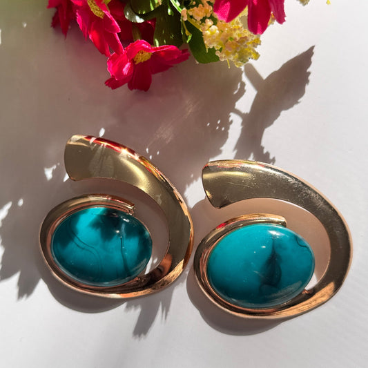 Exquisite gold and turquoise statement earrings, a perfect blend of elegance and boldness. Designed with a unique swirl-inspired gold frame, these earrings showcase a stunning oval turquoise stone with natural marbled veins, adding a touch of bohemian luxury. Whether you're dressing up for a special occasion or adding a chic accent to your everyday style, these earrings are the ultimate fashion-forward accessory. Vintage-inspired yet modern aesthetic.