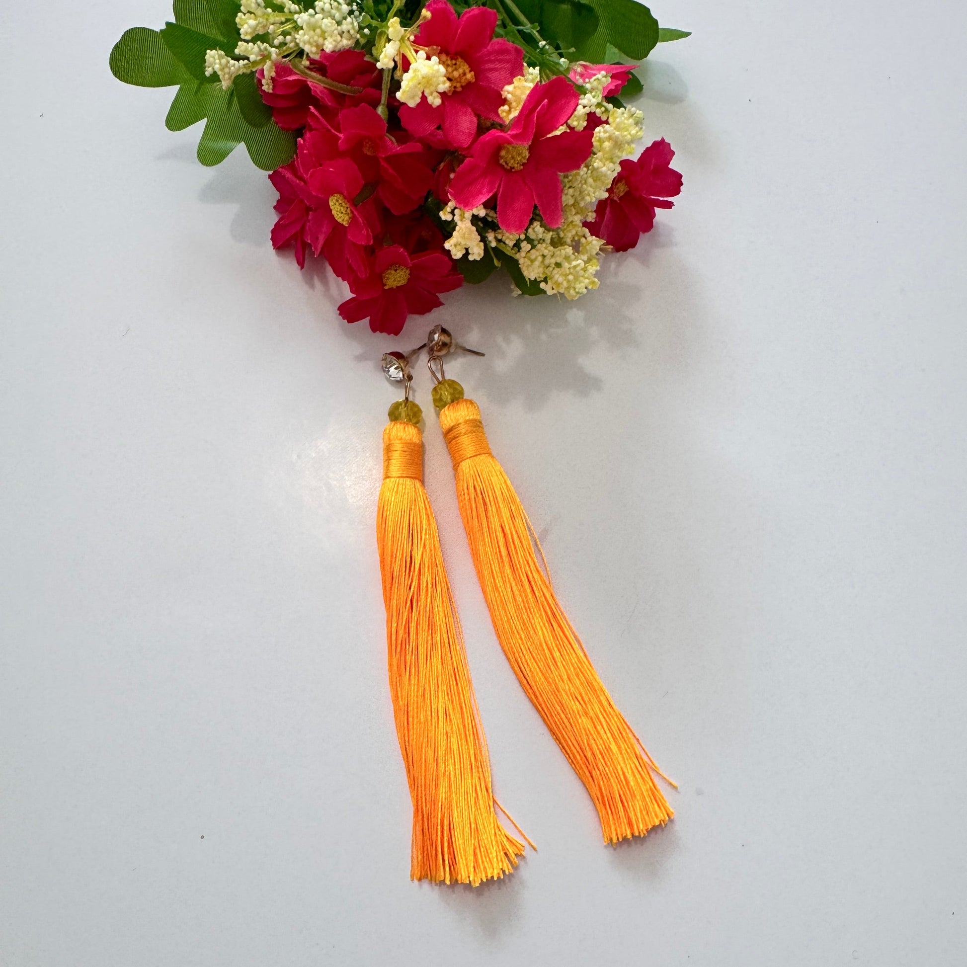 Turn heads with these stunning tassel earrings, designed to infuse your look with vibrant energy and effortless elegance. Featuring a mesmerizing shade of bold, sunshine-orange thread, these long, silky tassels sway gracefully with every movement, creating a captivating effect. Accentuated by delicate golden-hued beads and a sleek metallic stud, these earrings are the perfect statement piece for anyone who loves bold, eye-catching accessories. 