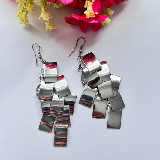 Elevate your style with these captivating silver statement earrings, designed to turn heads with their unique cascading geometric design. Crafted with a dynamic arrangement of reflective metallic squares, they catch the light with every movement, creating an irresistible shimmer. These ultra-chic dangles exude modern elegance with a touch of edgy sophistication, making them the perfect accessory for any occasion, from glamorous nights out to stylish daytime looks. 