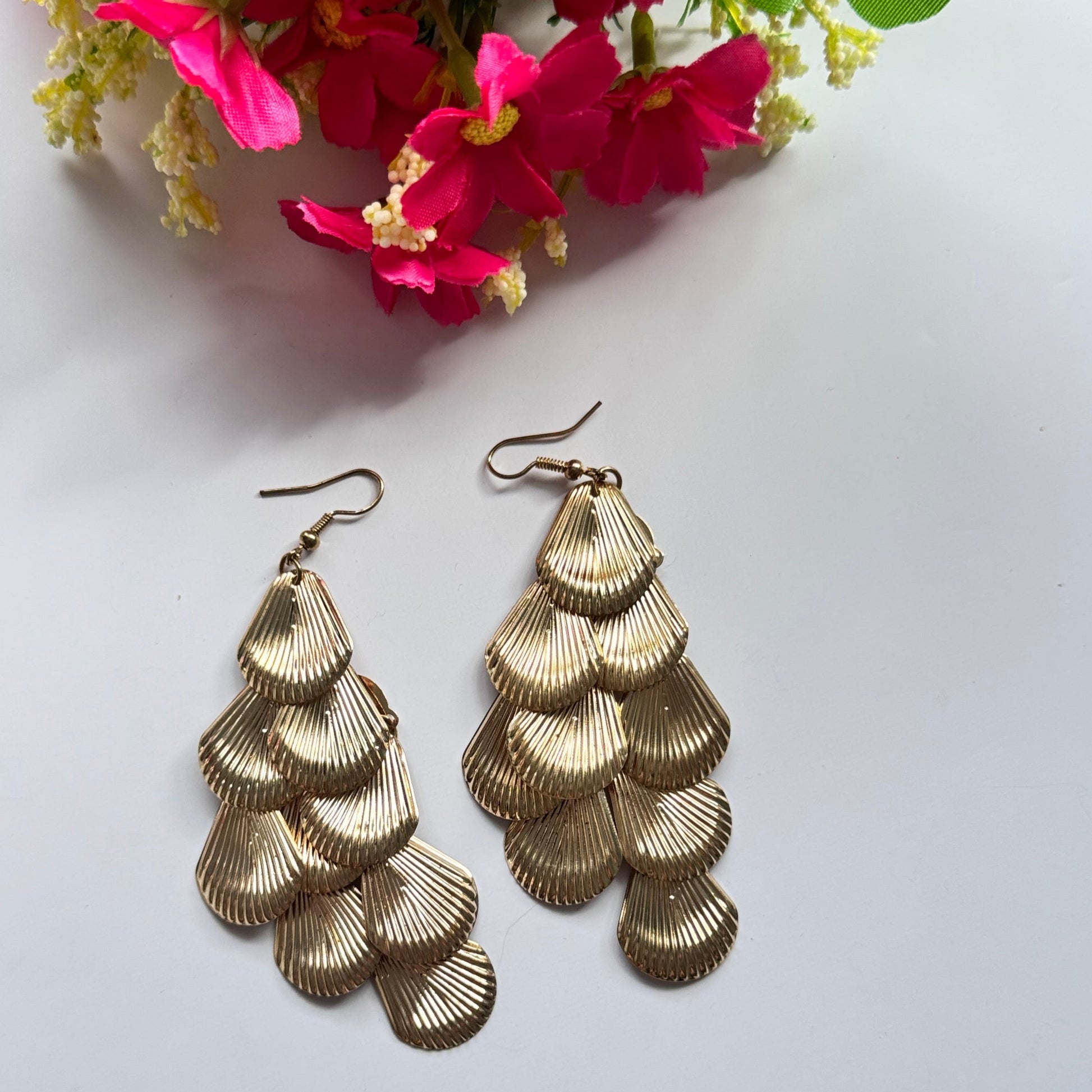 Introducing our Golden Cascade Shell Earrings, a stunning statement piece inspired by the elegance of ocean waves and timeless luxury. Designed with multiple layers of delicately textured, fan-shaped golden charms, these earrings create a mesmerizing waterfall effect that catches the light with every movement.