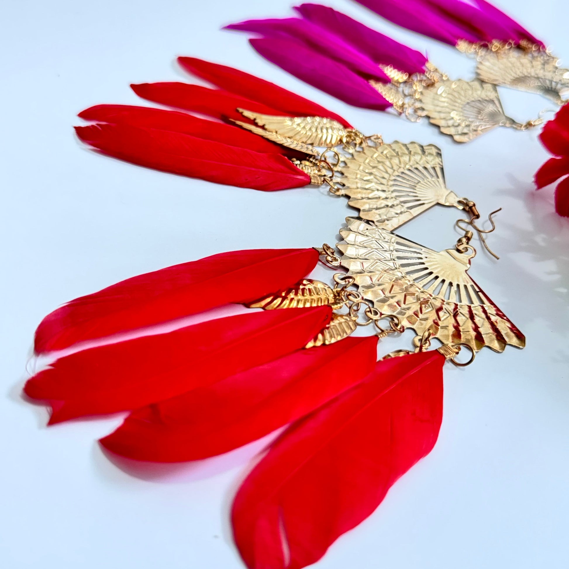  These breathtaking fan-shaped gold earrings feature intricate detailing, exuding a luxurious charm that captivates at first glance. Adorned with vibrant feather accents in striking red and fuchsia hues, they add a dramatic flair to any outfit, making them perfect for fashion-forward people who love to stand out. 