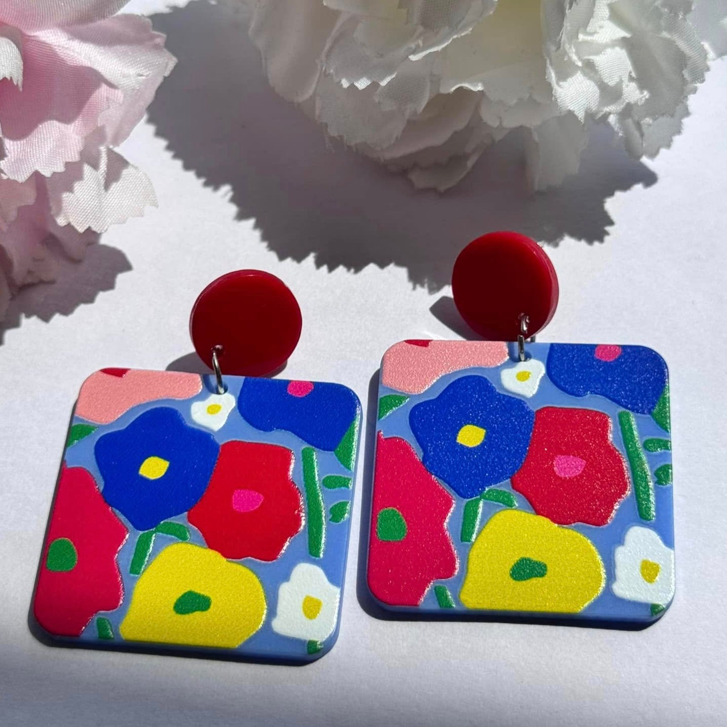Add a vibrant pop of color to your look with these hand-painted floral statement earrings, designed to bring out your bold and artistic side. Featuring a striking blend of red, blue, yellow, and green hues, these lightweight accessories are perfect for those who love to stand out. The playful yet sophisticated square design, paired with glossy red studs, creates a modern, artsy appeal that complements any outfit effortlessly. 