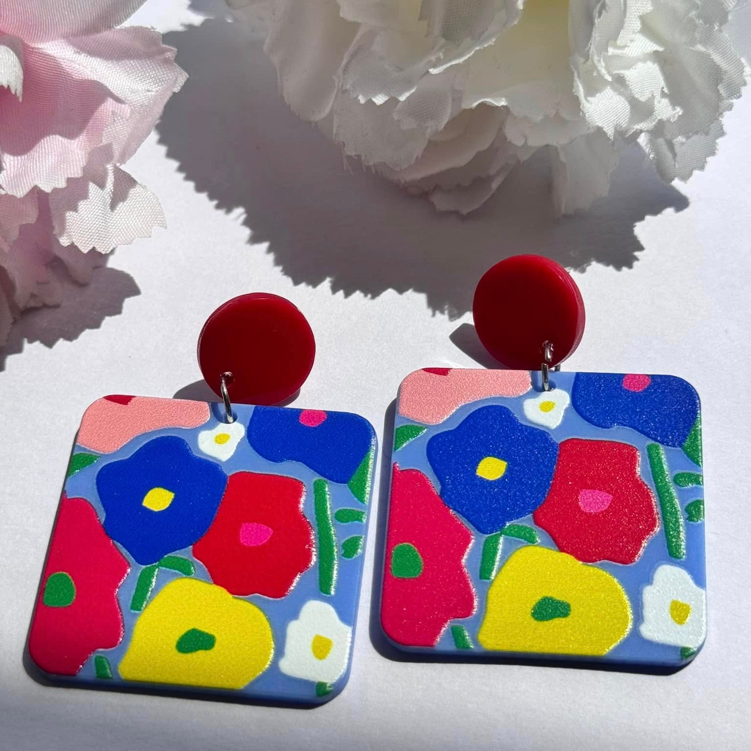 Add a vibrant pop of color to your look with these hand-painted floral statement earrings, designed to bring out your bold and artistic side. Featuring a striking blend of red, blue, yellow, and green hues, these lightweight accessories are perfect for those who love to stand out. The playful yet sophisticated square design, paired with glossy red studs, creates a modern, artsy appeal that complements any outfit effortlessly. 