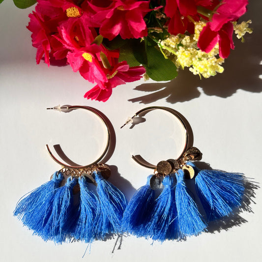 The ultimate statement accessory that effortlessly blends bold elegance with a touch of playful charm! Crafted with sleek gold-tone hoops, these earrings feature a cascade of rich, blue tassels, each adorned with delicate golden coin accents for a hint of shimmer. 