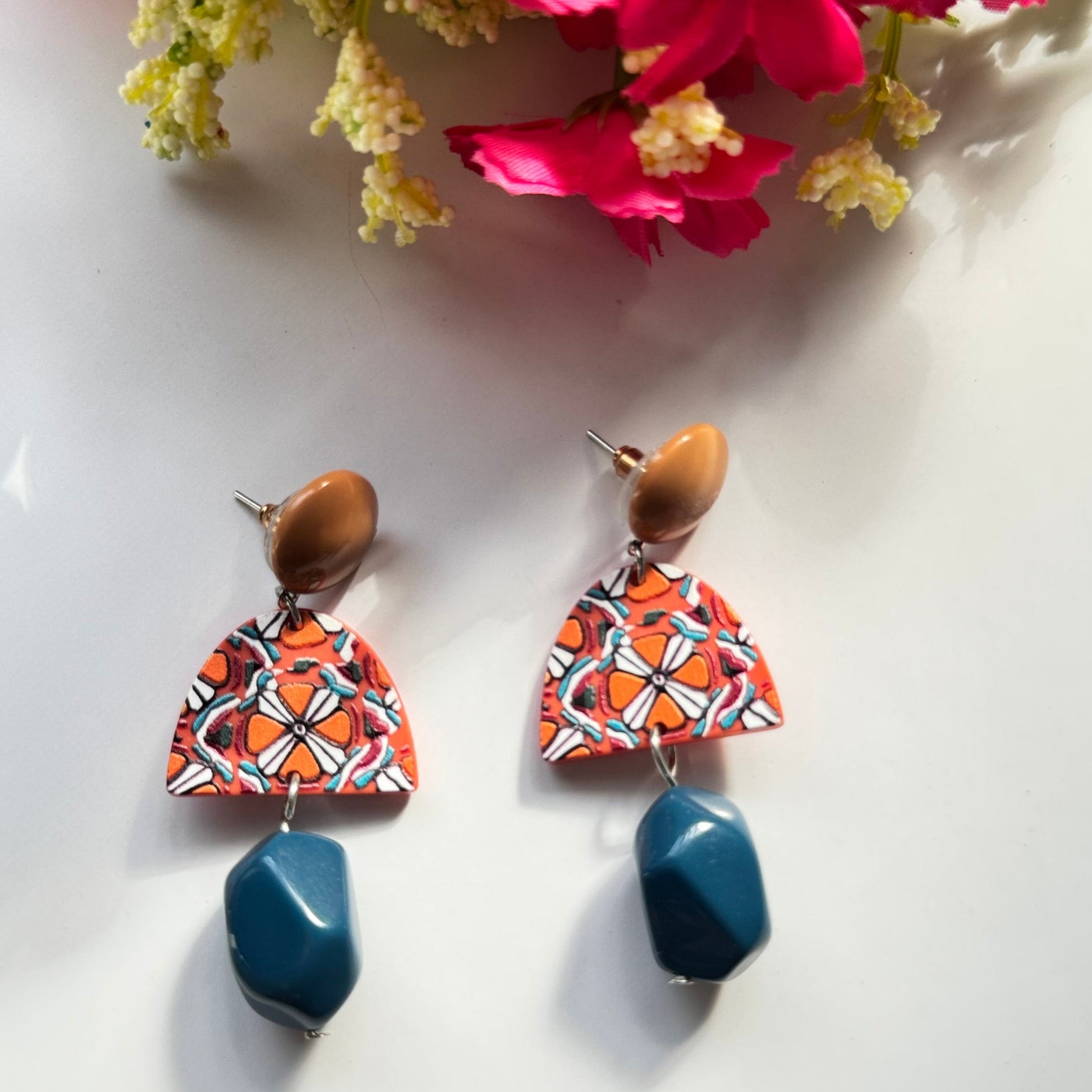 Add a bold statement to your style with these statement earrings, designed to captivate attention with their unique fusion of earthy tones and vibrant artistry. Featuring a warm caramel-toned stud, a geometric charm with intricate patterns in fiery orange, white, and black, and a deep blue faceted bead that adds a touch of sophistication, these earrings are a masterpiece of color harmony and texture. Lightweight yet impactful, they bring a perfect balance of modern elegance and artistic flair to any outfit.