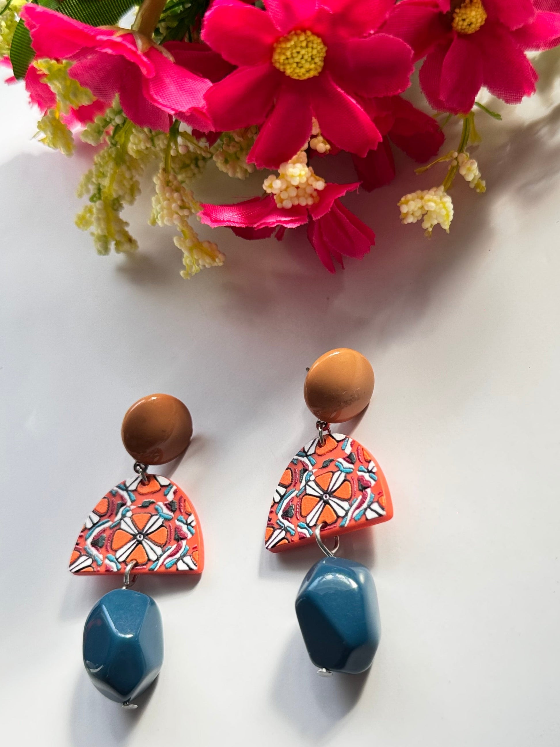 Add a bold statement to your style with these statement earrings, designed to captivate attention with their unique fusion of earthy tones and vibrant artistry. Featuring a warm caramel-toned stud, a geometric charm with intricate patterns in fiery orange, white, and black, and a deep blue faceted bead that adds a touch of sophistication, these earrings are a masterpiece of color harmony and texture. Lightweight yet impactful, they bring a perfect balance of modern elegance and artistic flair to any outfit.
