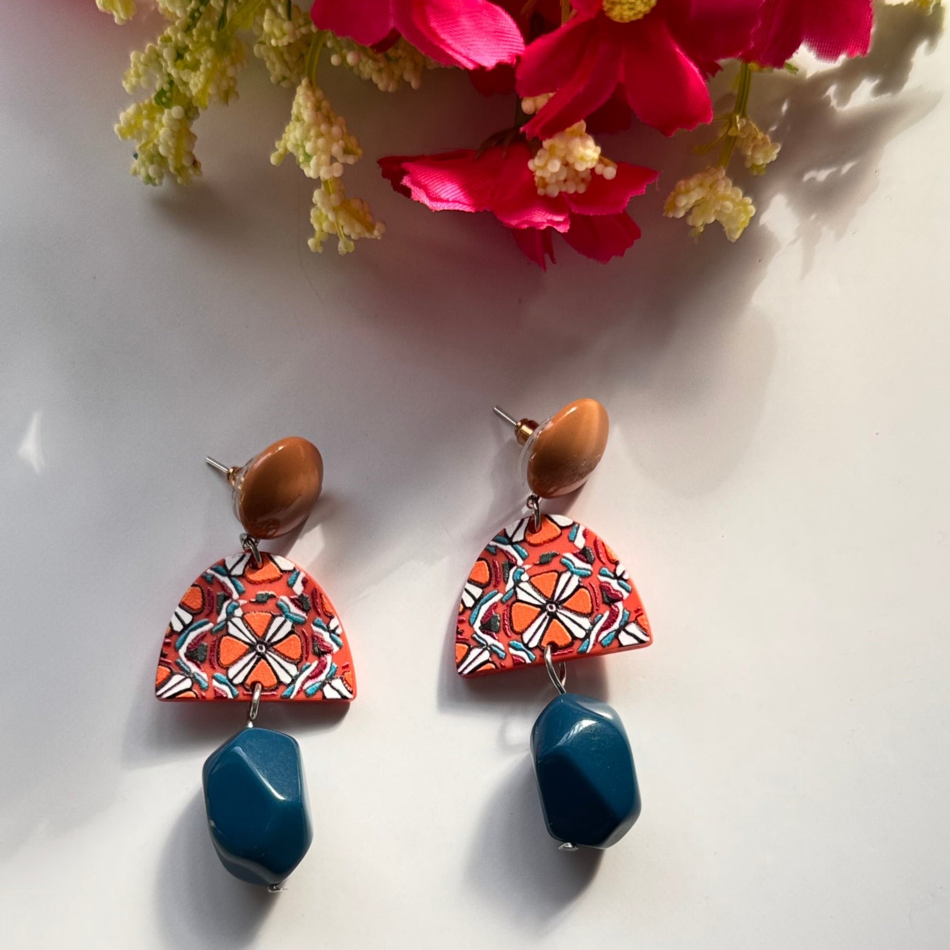 Add a bold statement to your style with these statement earrings, designed to captivate attention with their unique fusion of earthy tones and vibrant artistry. Featuring a warm caramel-toned stud, a geometric charm with intricate patterns in fiery orange, white, and black, and a deep blue faceted bead that adds a touch of sophistication, these earrings are a masterpiece of color harmony and texture. Lightweight yet impactful, they bring a perfect balance of modern elegance and artistic flair to any outfit.
