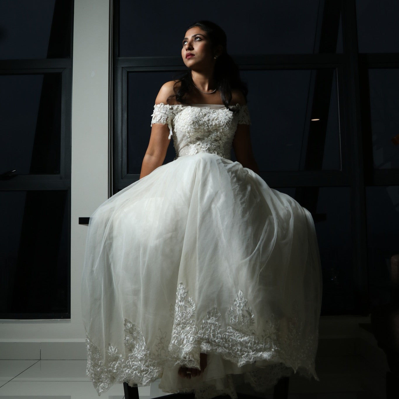 This dress is a stunning off-shoulder bridal gown with intricate lace detailing and a flowing tulle skirt. The bodice features delicate floral appliqués that add a touch of elegance, while the off-shoulder design enhances its romantic appeal. The lightweight fabric and airy structure make it an excellent choice for an outdoor or beach wedding, offering both comfort and grace. 