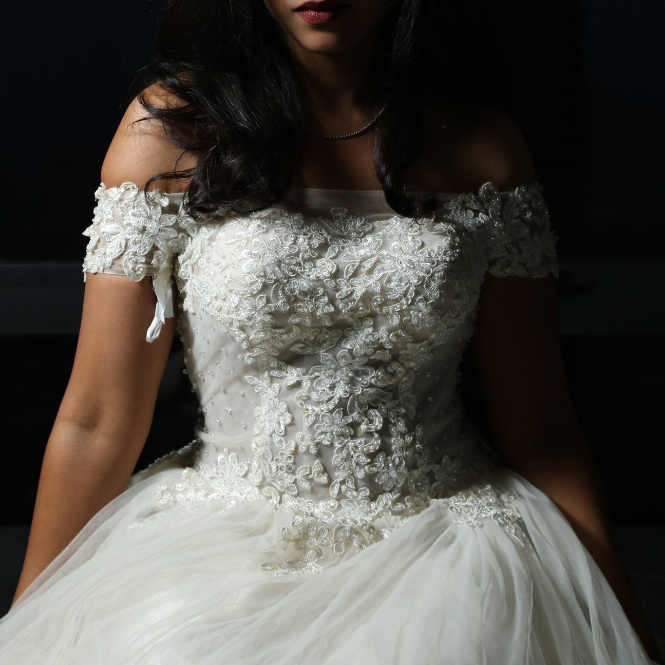 This dress is a stunning off-shoulder bridal gown with intricate lace detailing and a flowing tulle skirt. The bodice features delicate floral appliqués that add a touch of elegance, while the off-shoulder design enhances its romantic appeal. The lightweight fabric and airy structure make it an excellent choice for an outdoor or beach wedding, offering both comfort and grace. 