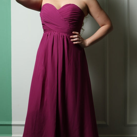 This elegant strapless gown features a beautifully ruched bodice and a flowing A-line skirt, creating a timeless and flattering silhouette. The rich magenta color adds a bold and sophisticated touch, perfect for formal events, bridesmaids, or special occasions. Crafted from lightweight fabric, it offers both comfort and style for an effortlessly graceful look.