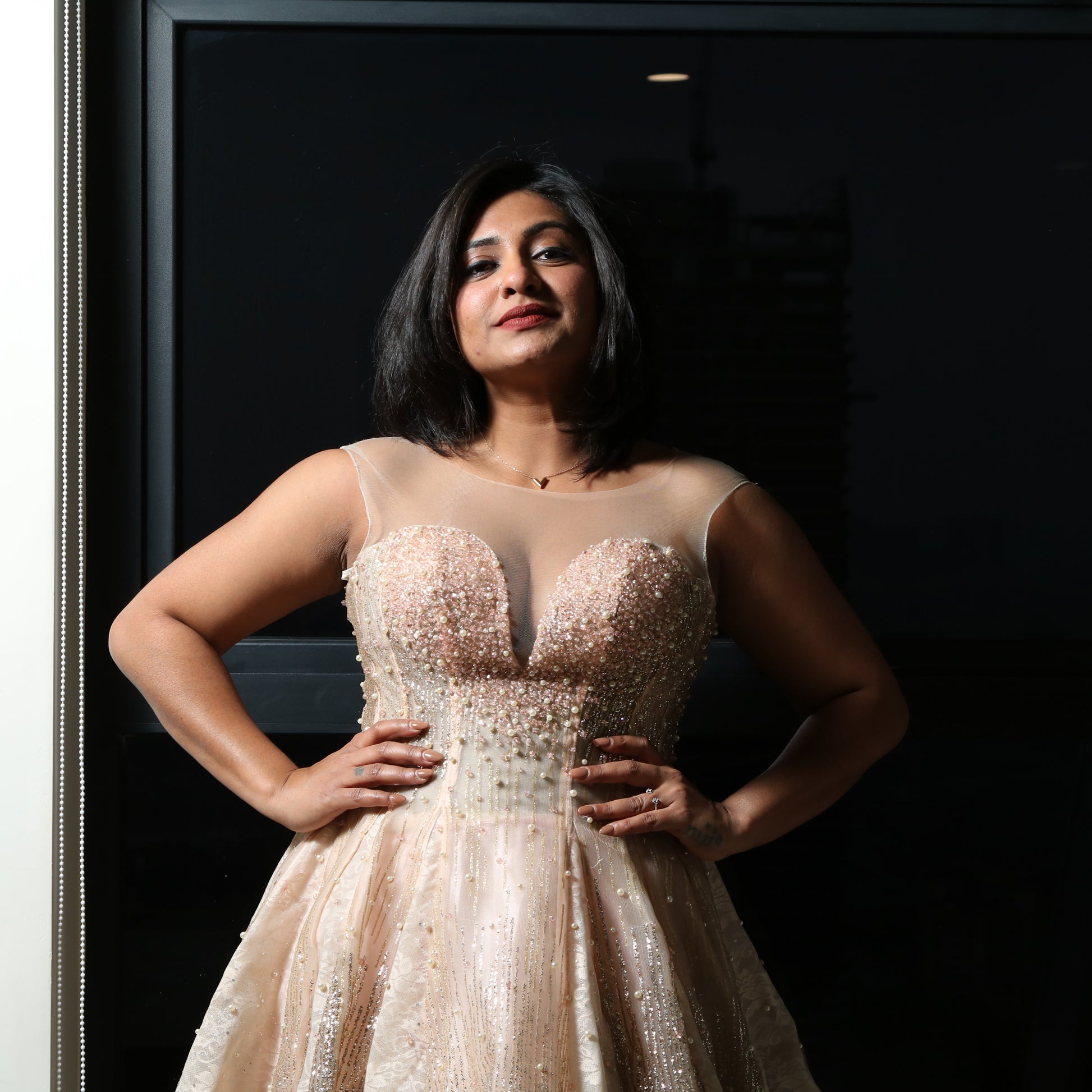 The dress in the image is an elegant, heavily embellished gown with a fitted bodice and a voluminous skirt. It features intricate beadwork and embroidery, giving it a luxurious and opulent look. The sheer illusion neckline adds a delicate touch, while the structured, corset-like bodice enhances the silhouette. The fabric appears to be thick and richly adorned, making the dress quite heavy. The overall design exudes a regal and glamorous feel, perfect for a formal event or gala.